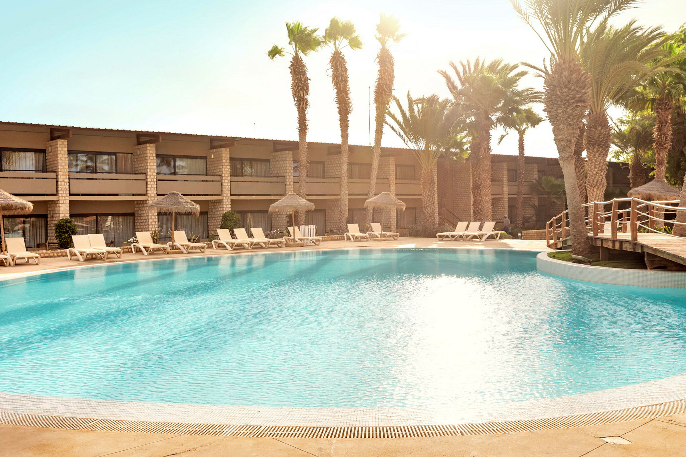 En pool omgiven av solstolar och palmer vid ett hotell. (AI-genererad text)