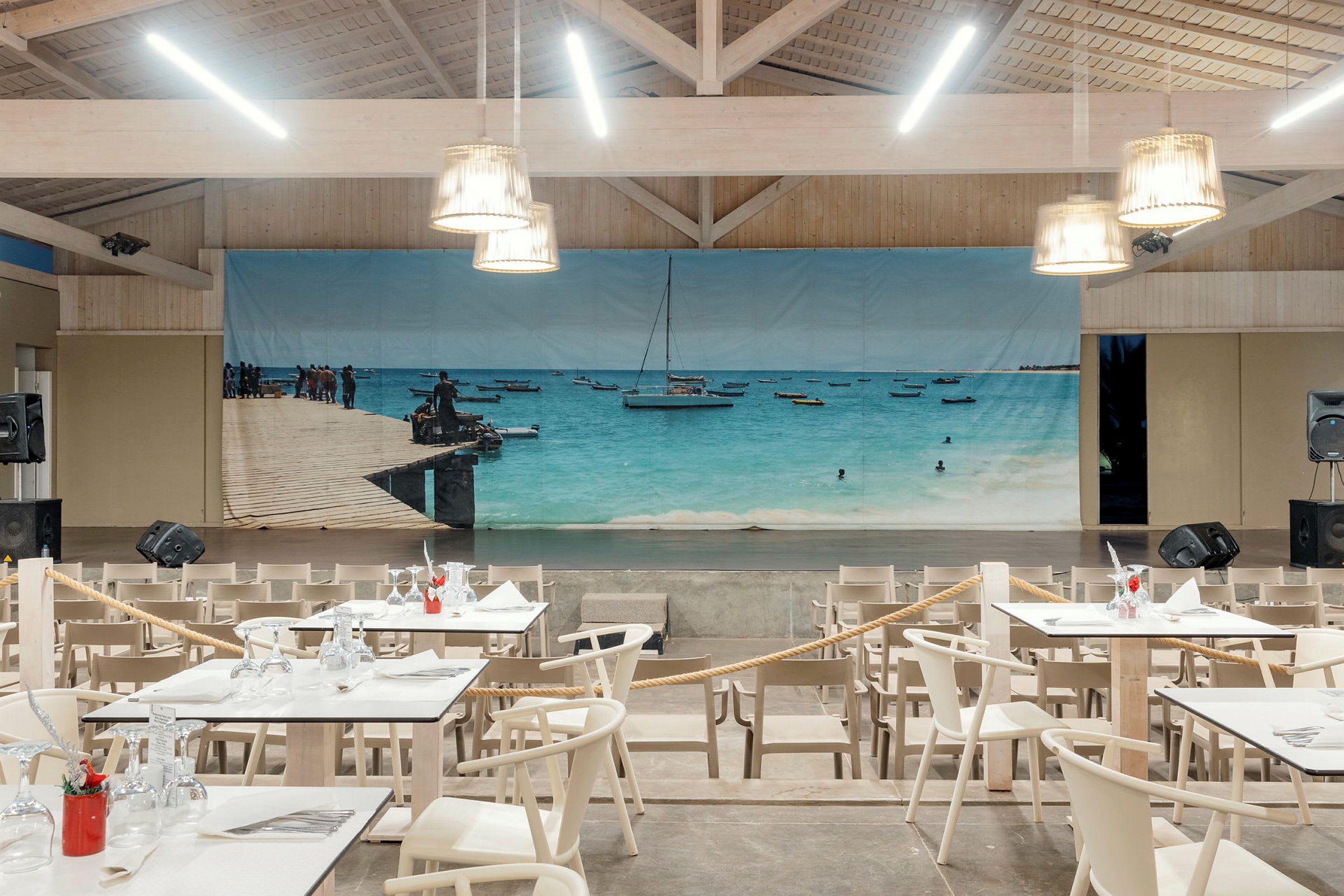 Interiör med bord och stolar framför en scen dekorerad med en strandbild. (AI-genererad text)