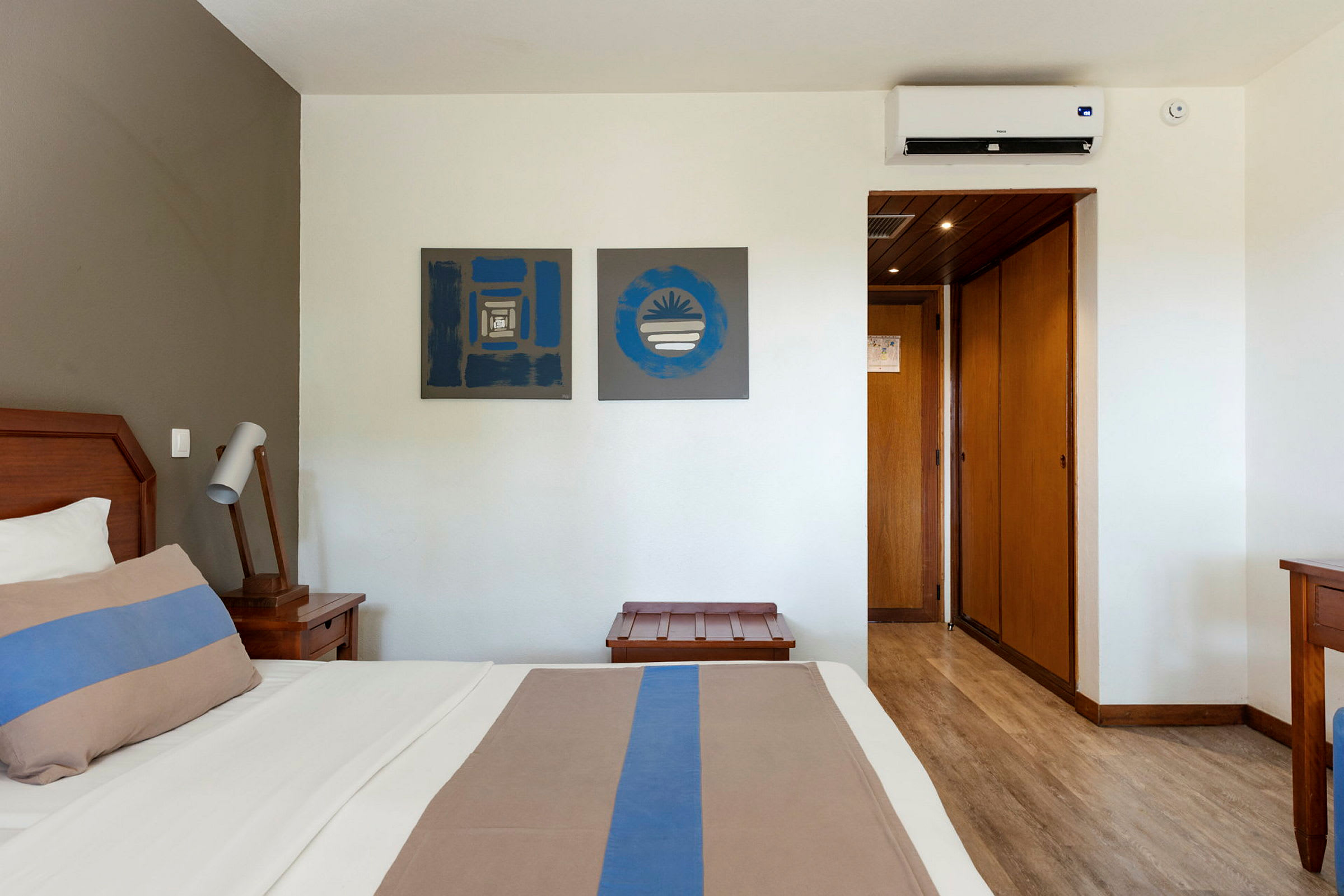 Hotellrum med säng, sängbord, konst på väggarna och en luftkonditioneringsenhet. (AI-genererad text)