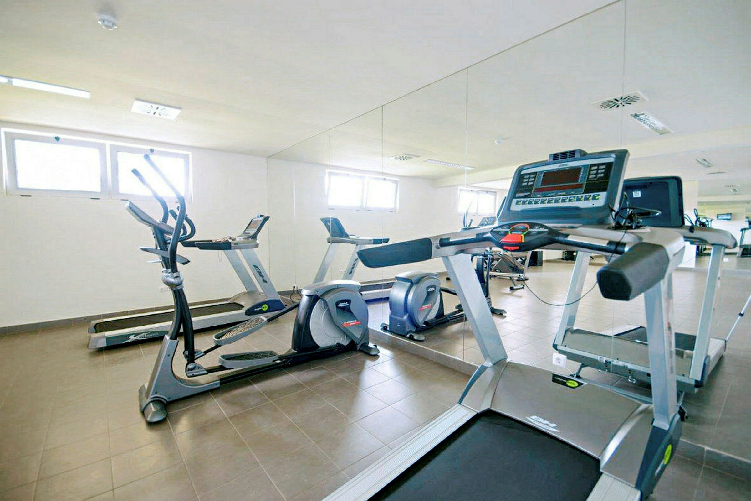 Bild av ett gym med träningsutrustning inklusive löpband och elliptiska maskiner framför en spegel. (AI-genererad text)