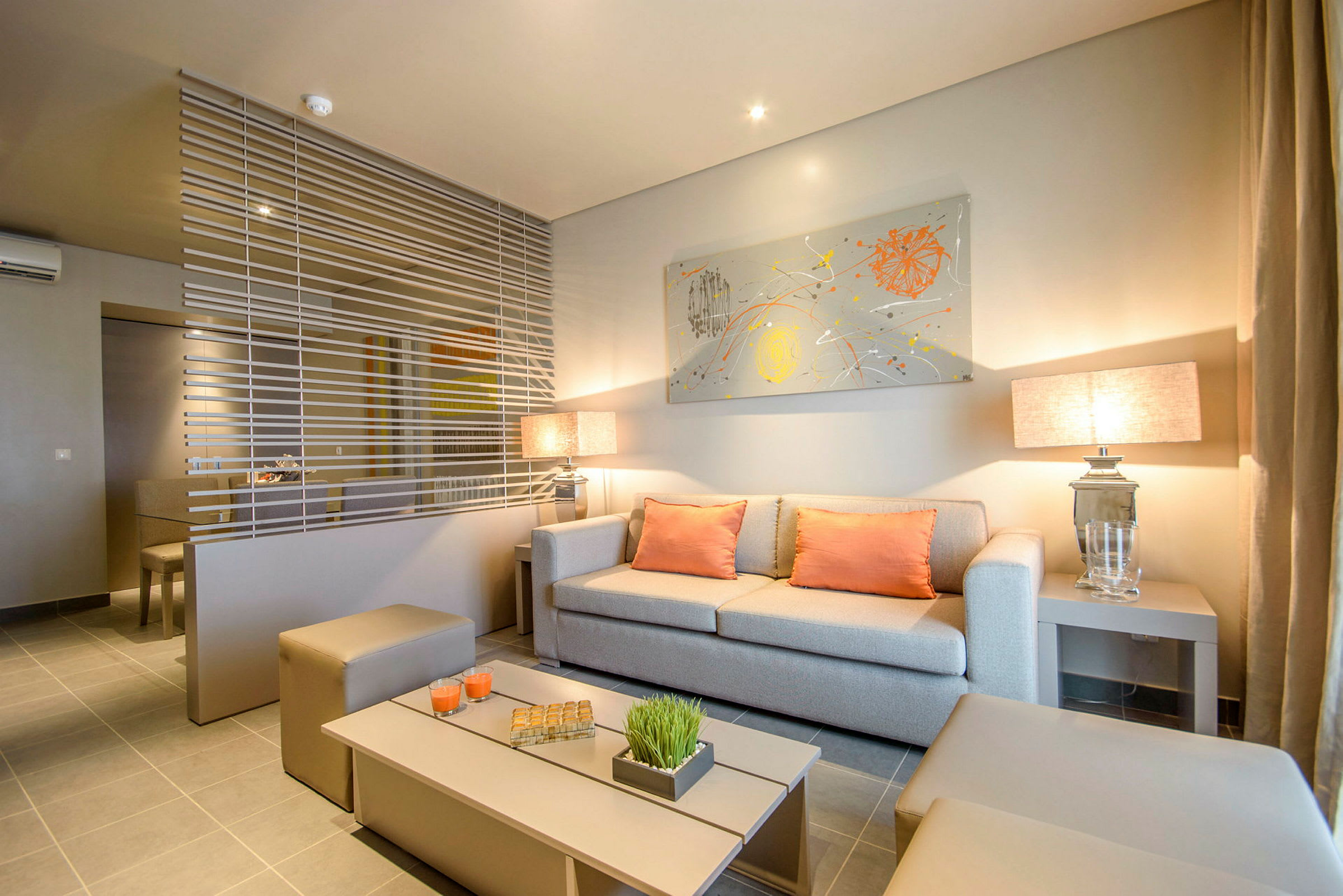 Vardagsrum med modern inredning, beige soffa och orange kuddar, avdelat med dekorativt horisontellt nät. (AI-genererad text)