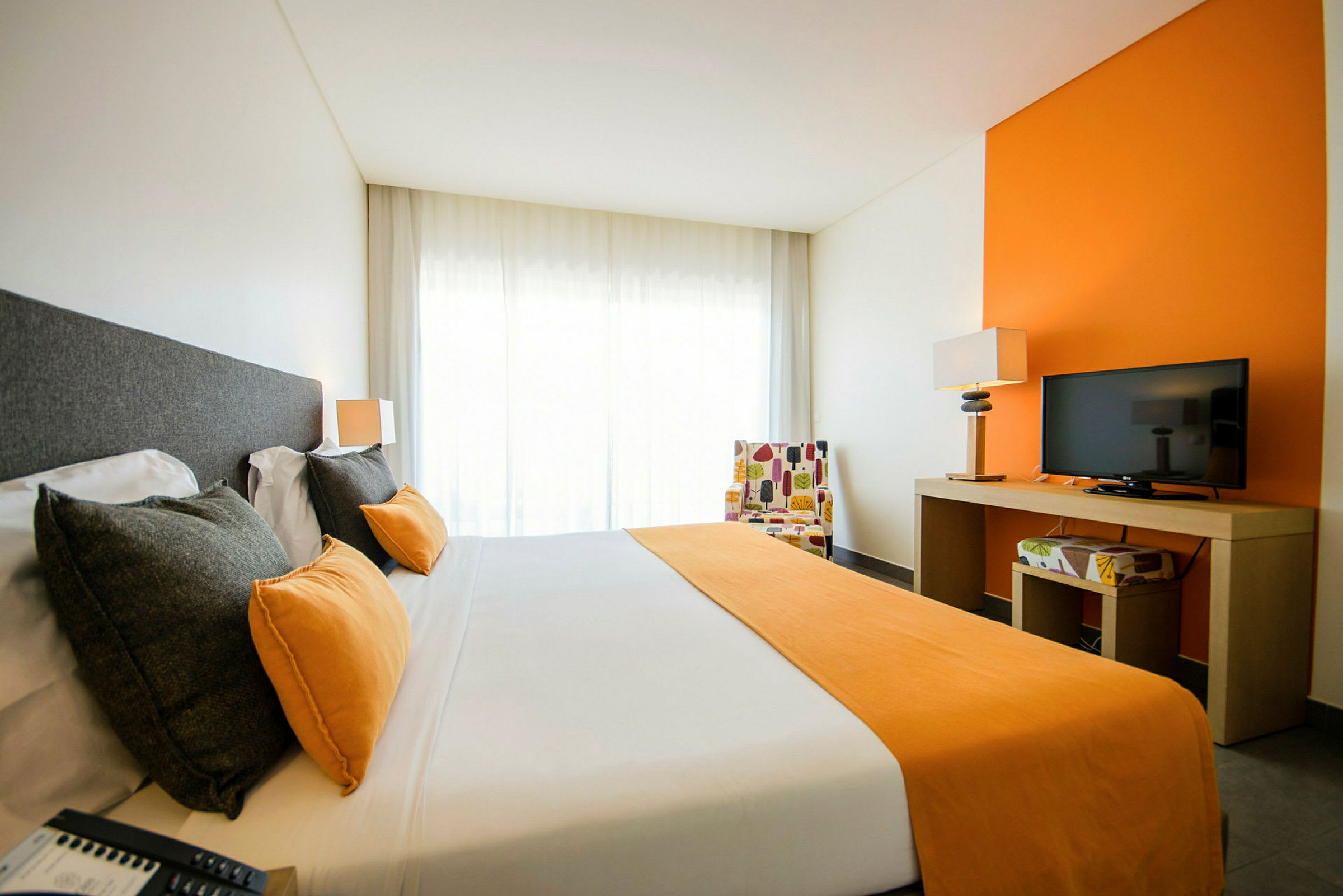 Bild på ett hotellrum med en dubbelsäng, orange detaljer och en tv på ett bord. (AI-genererad text)