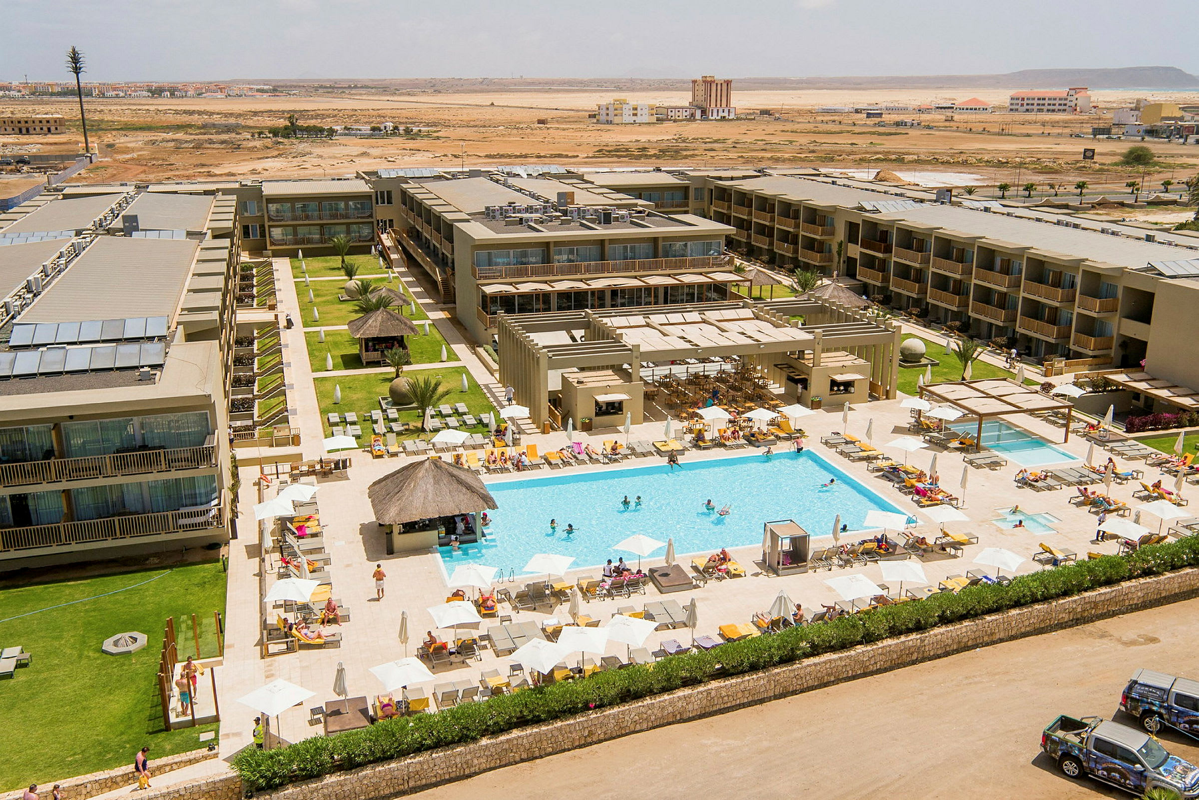Ett hotellkomplex med en stor swimmingpool omgiven av solstolar och parasoller. (AI-genererad text)