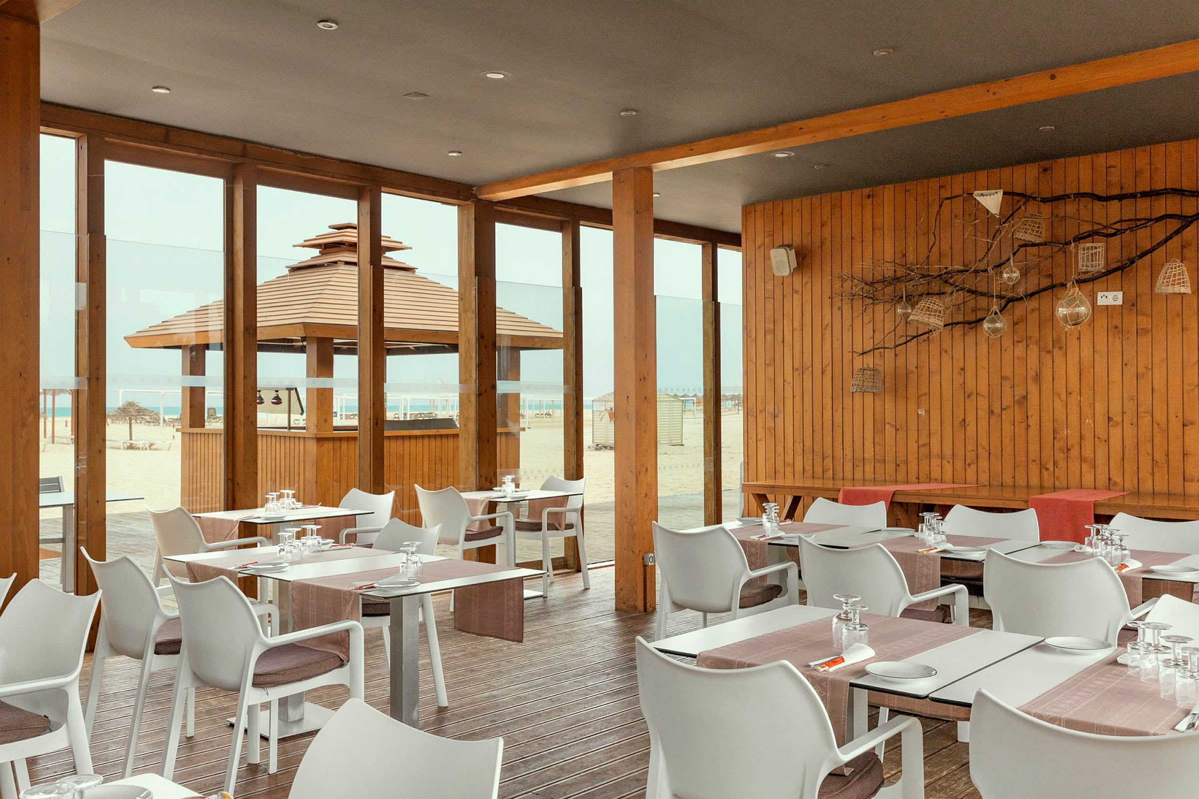 Restaurang med träpanel och glasväggar med utsikt över stranden. (AI-genererad text)