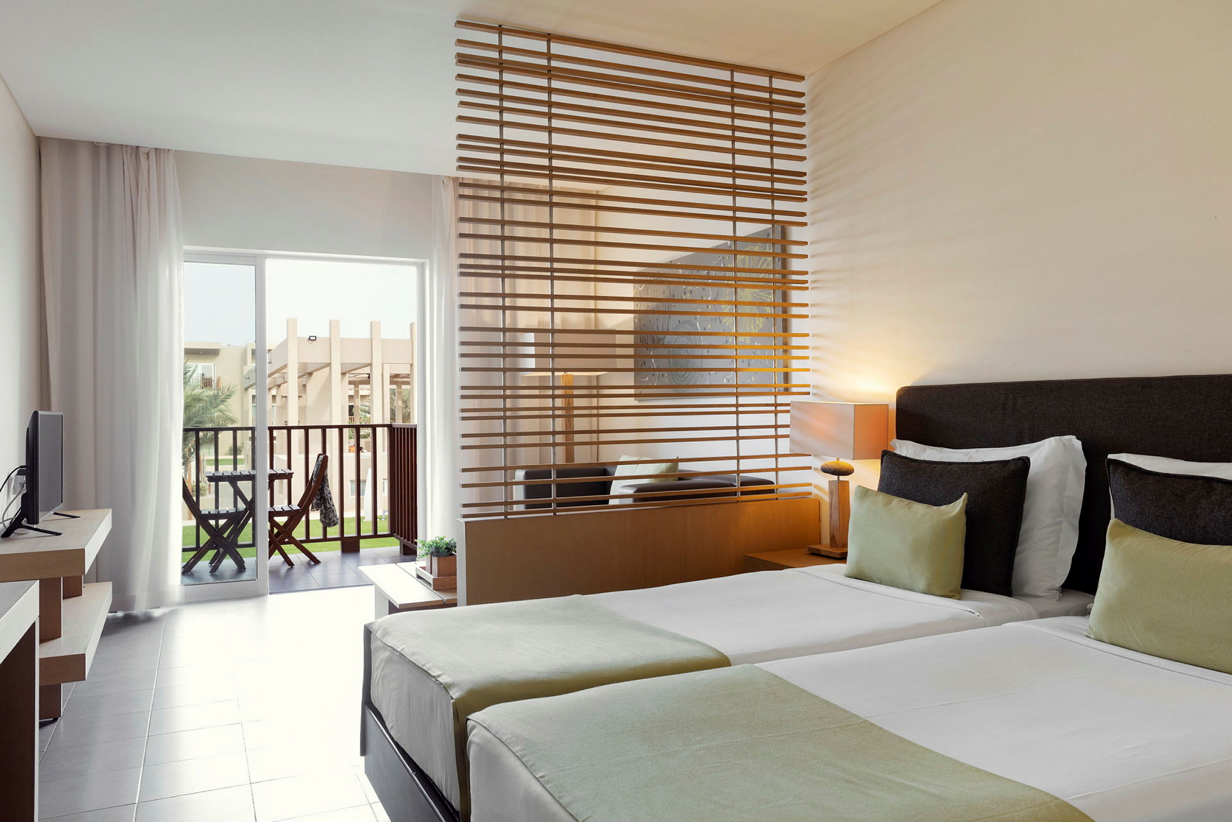 Hotellrum med två enkelsängar, en sittplats med en avdelare, och en terrass med utsikt. (AI-genererad text)