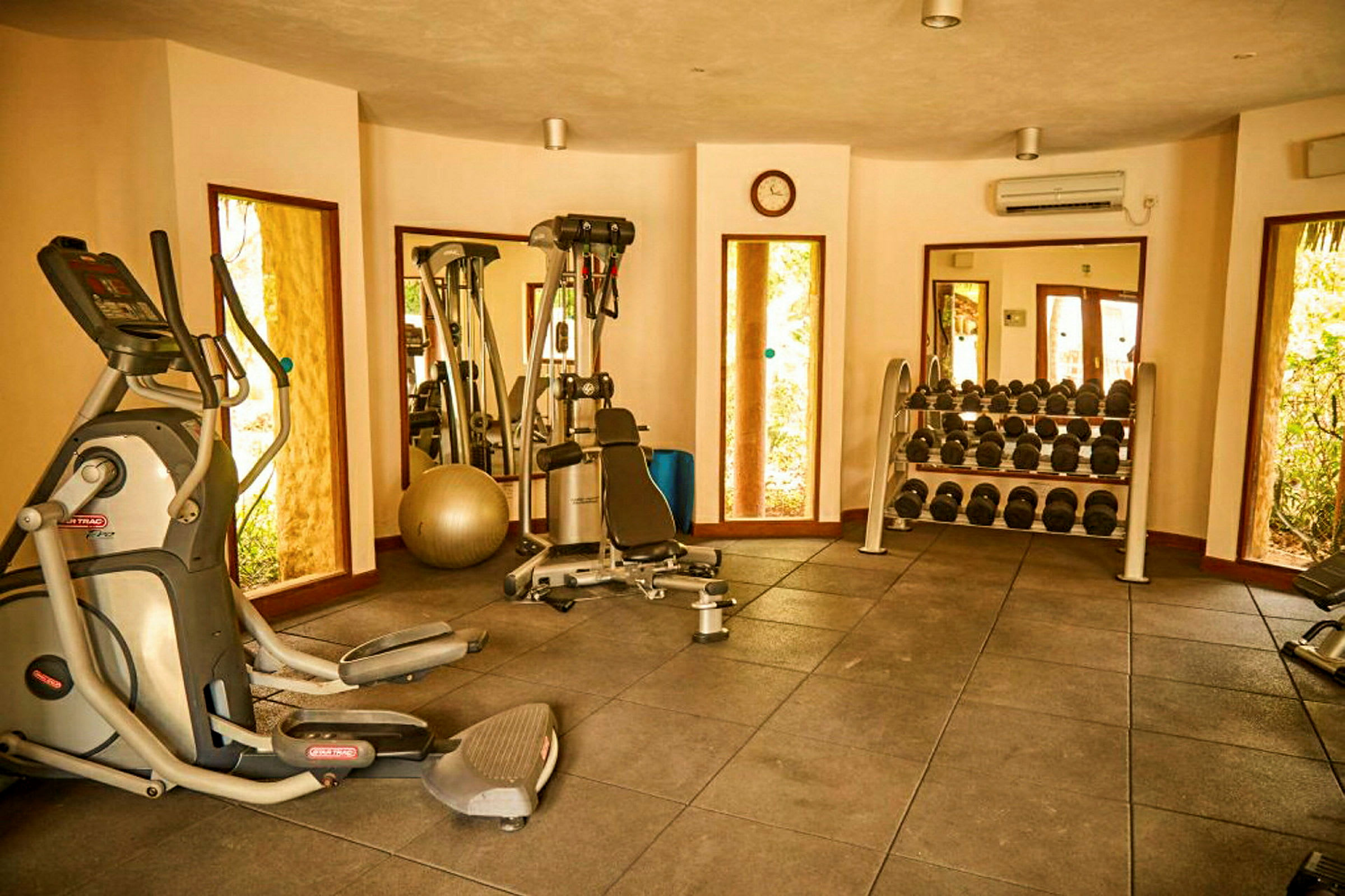 Ett gym med träningsmaskiner, speglar, en hylla med hantlar och en träningsboll. (AI-genererad text)