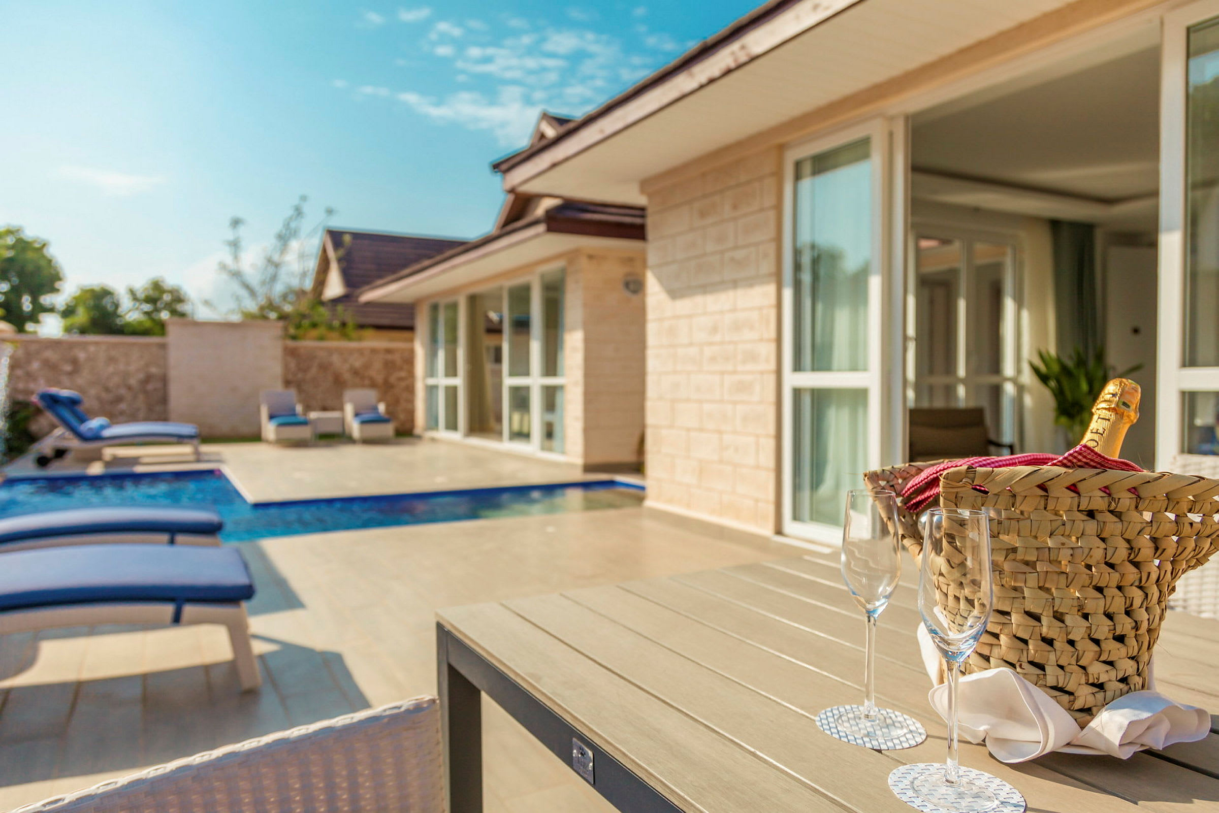 Ett lyxigt hus med pool och solstolar, samt ett bord med en champanjekorg och glas. (AI-genererad text)