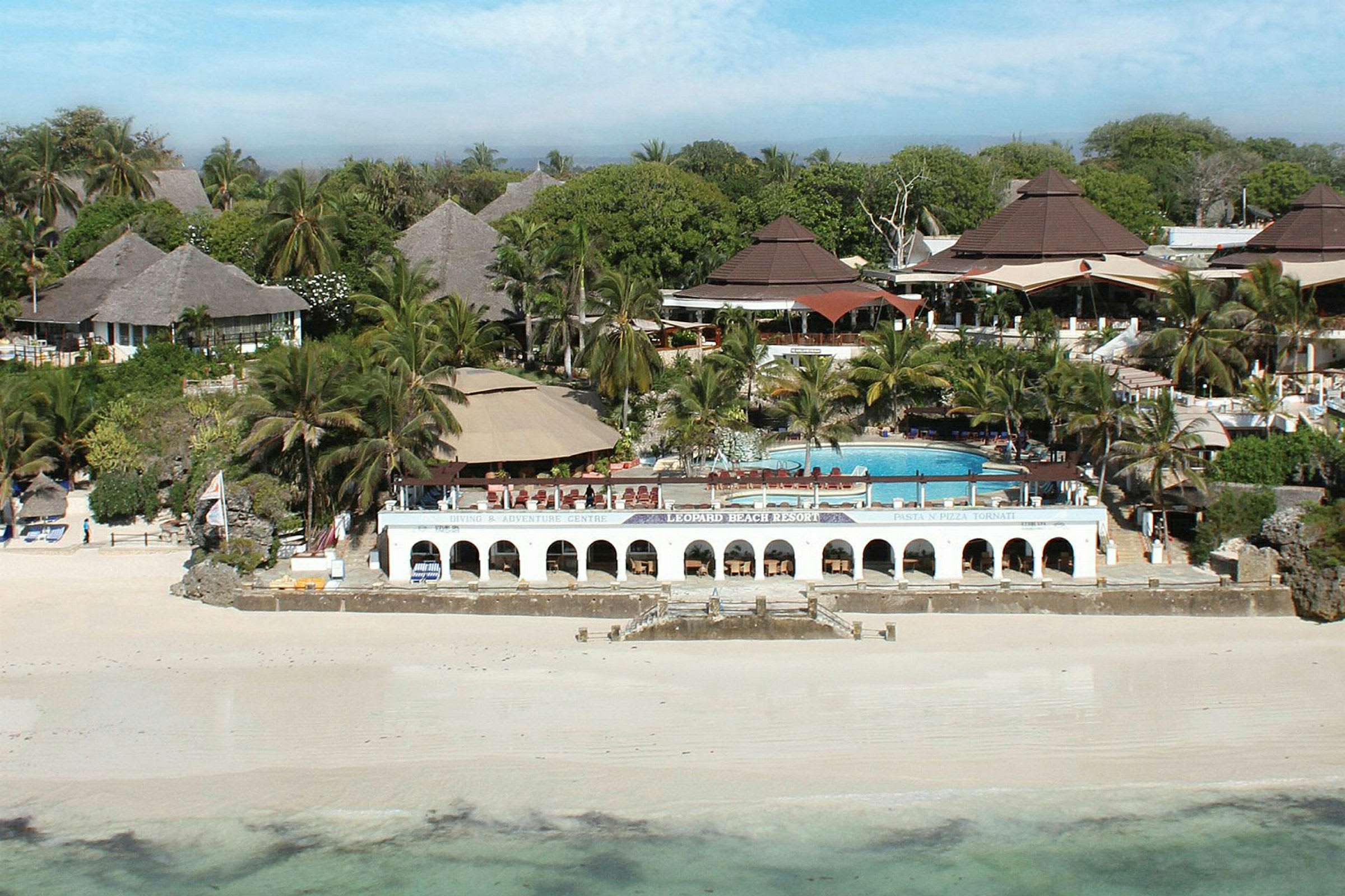 Ett strandresort med sandstrand, palmer, pool och bungalower. (AI-genererad text)