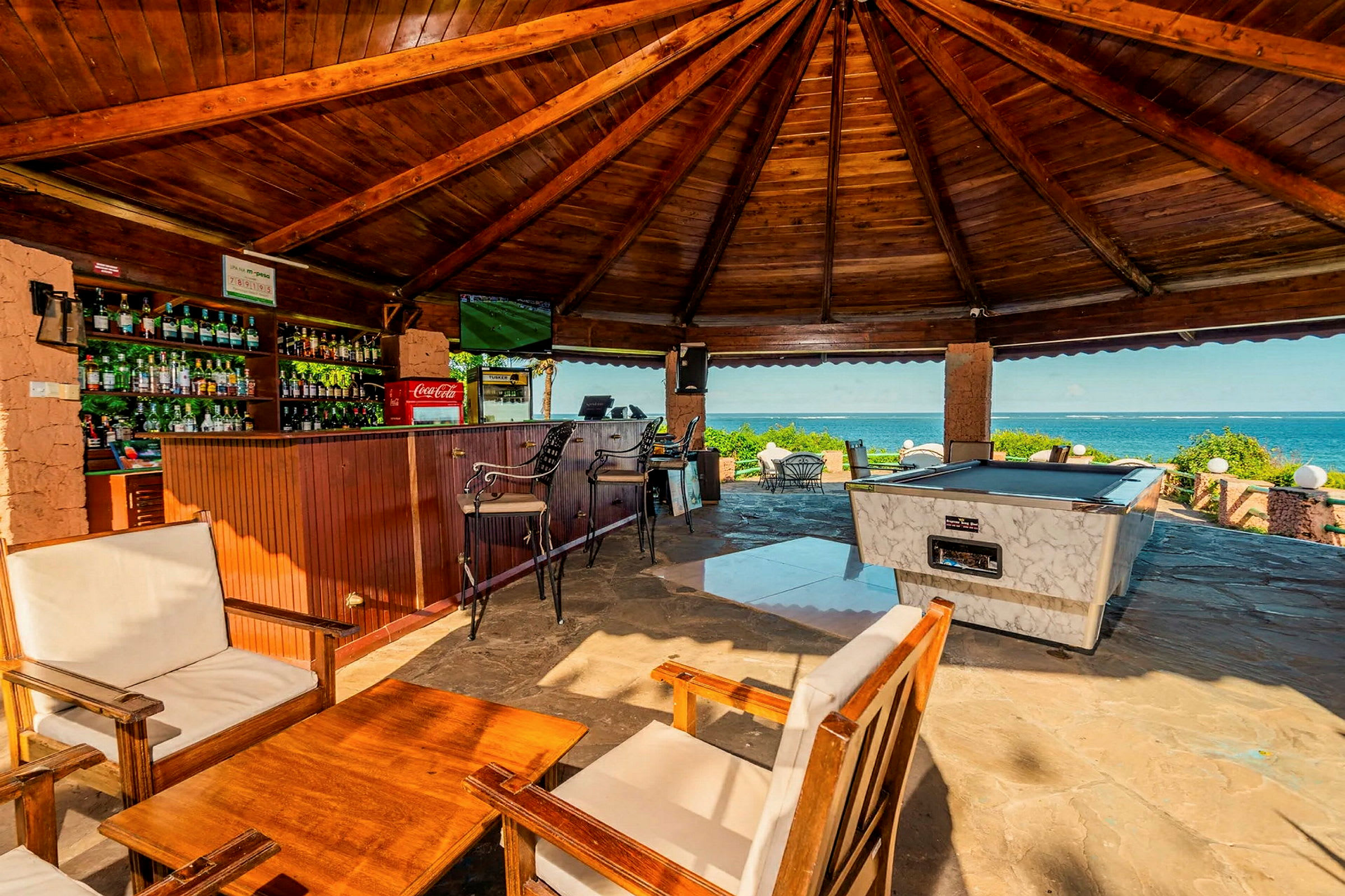 Ett uterum med träpanel, en bar, ett biljardbord och sittmöbler med utsikt över havet. (AI-genererad text)