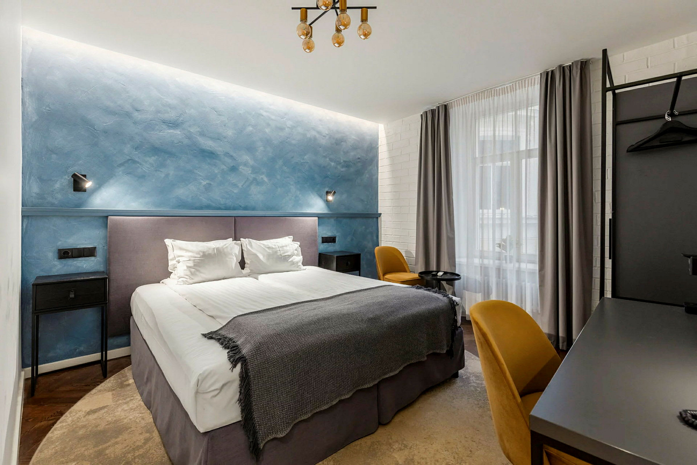 Ett hotellrum med en dubbelsäng, blå vägg och gula stolar. (AI-genererad text)