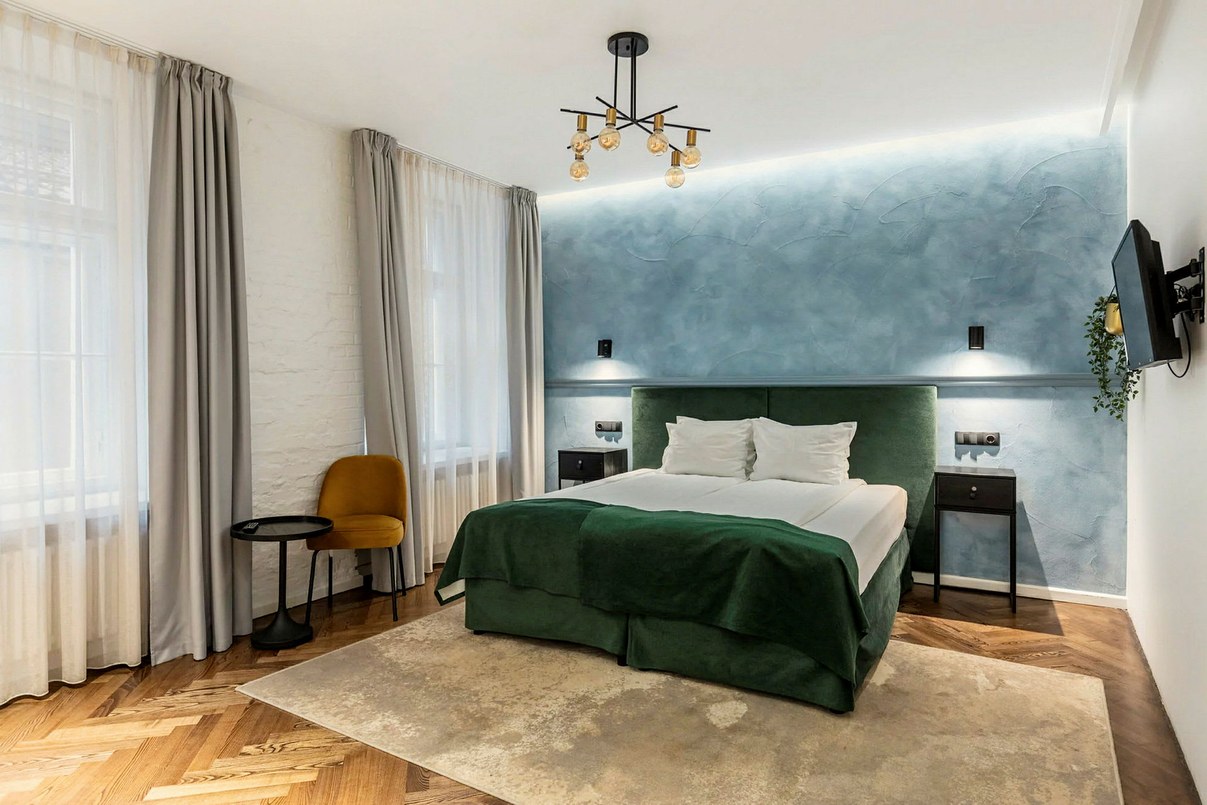 Ett stilrent hotellrum med dubbelsäng, blå vägg och gröna textilier. (AI-genererad text)