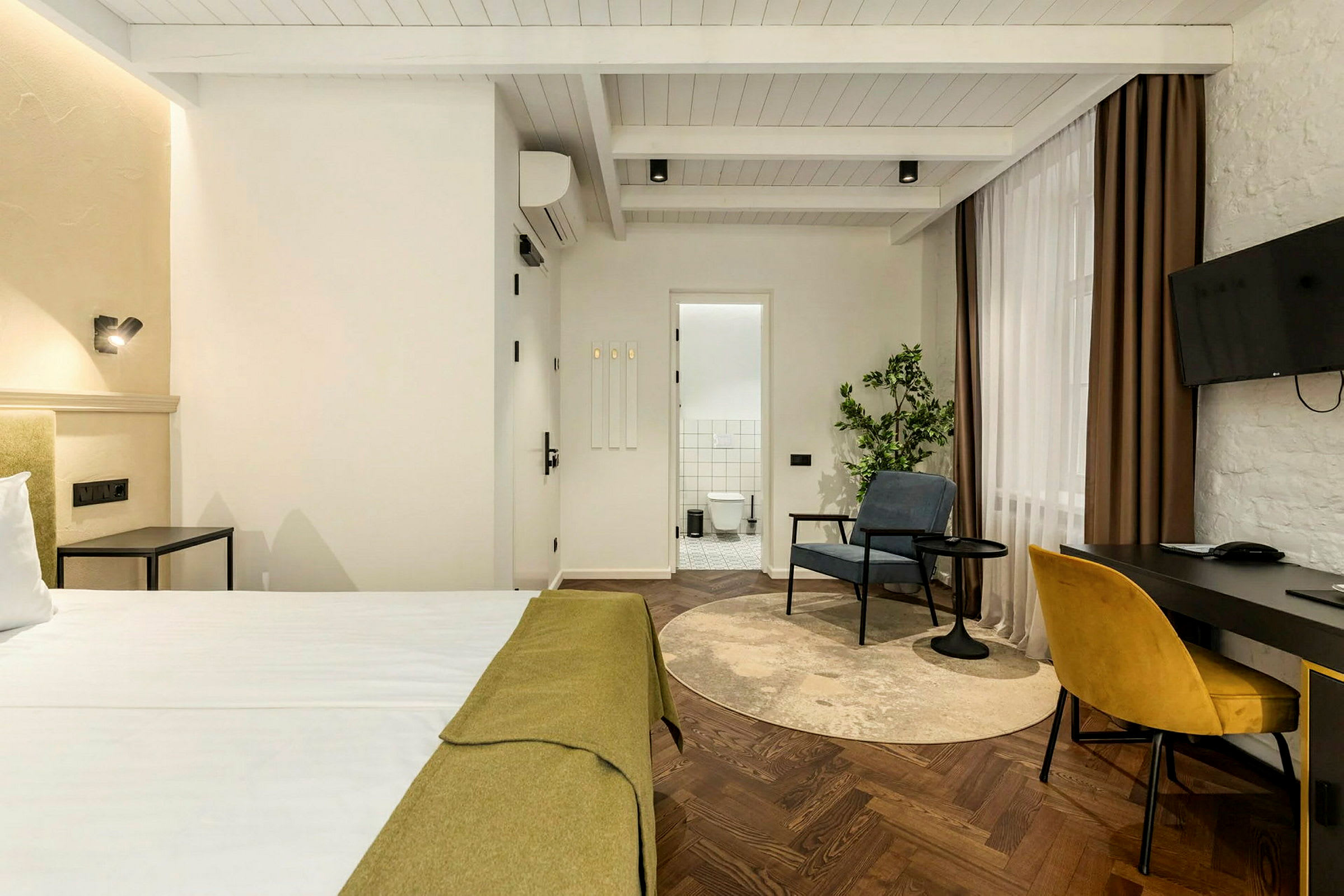 Ett hotellrum med en säng, ett skrivbord med stol, en fåtölj och ett badrum i bakgrunden. (AI-genererad text)