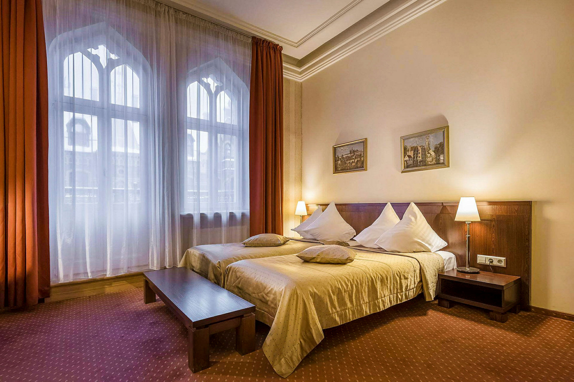 Ett hotellrum med två enkelsängar sammansatta, dekorerade med vita kuddar och beige sängkläder. Stora fönster med gardiner är placerade på vänster sida av rummet. (AI-genererad text)