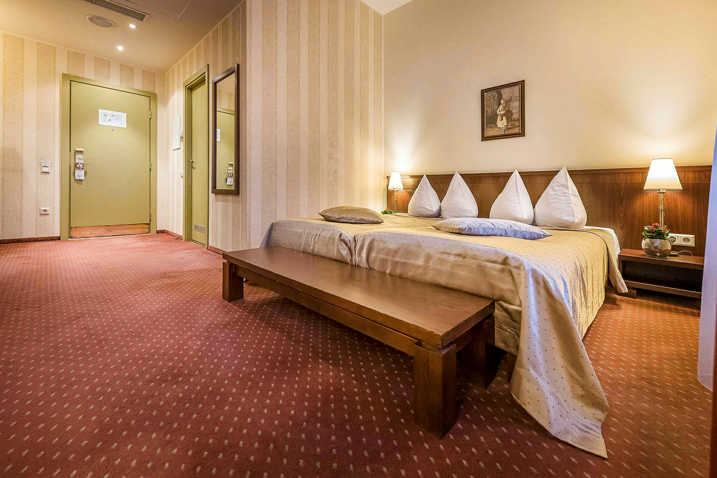 Ett hotellrum med en bäddad säng, en lång träbänk och dekorativa lampor. (AI-genererad text)