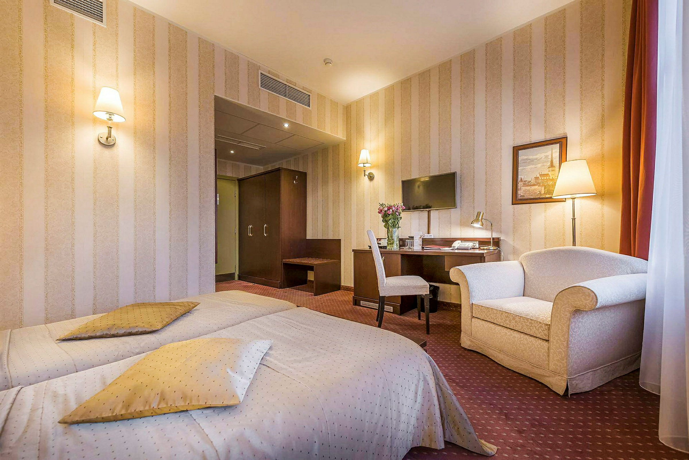 Hotellrum med två enkelsängar, skrivbord med stol, tv på väggen, och en fåtölj. (AI-genererad text)
