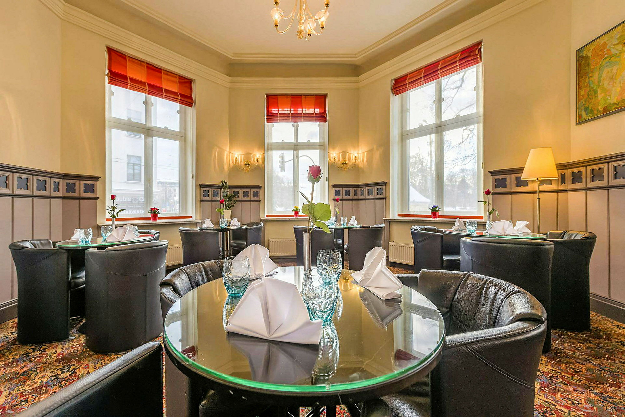 Interiör av en restaurang med dukade runda bord och stora fönster. (AI-genererad text)