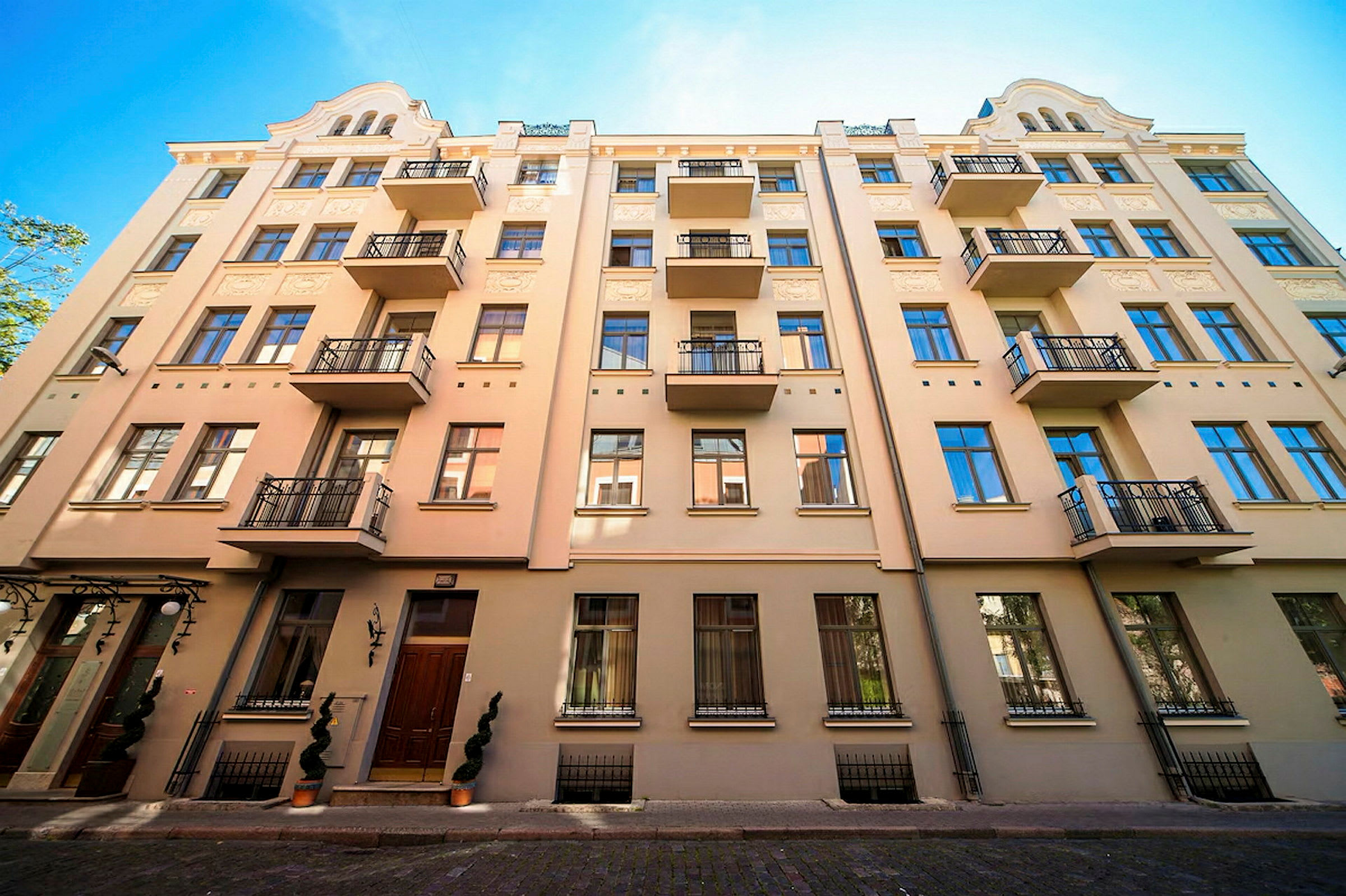 Fasad av en beige byggnad med flera balkonger och blå fönster. (AI-genererad text)