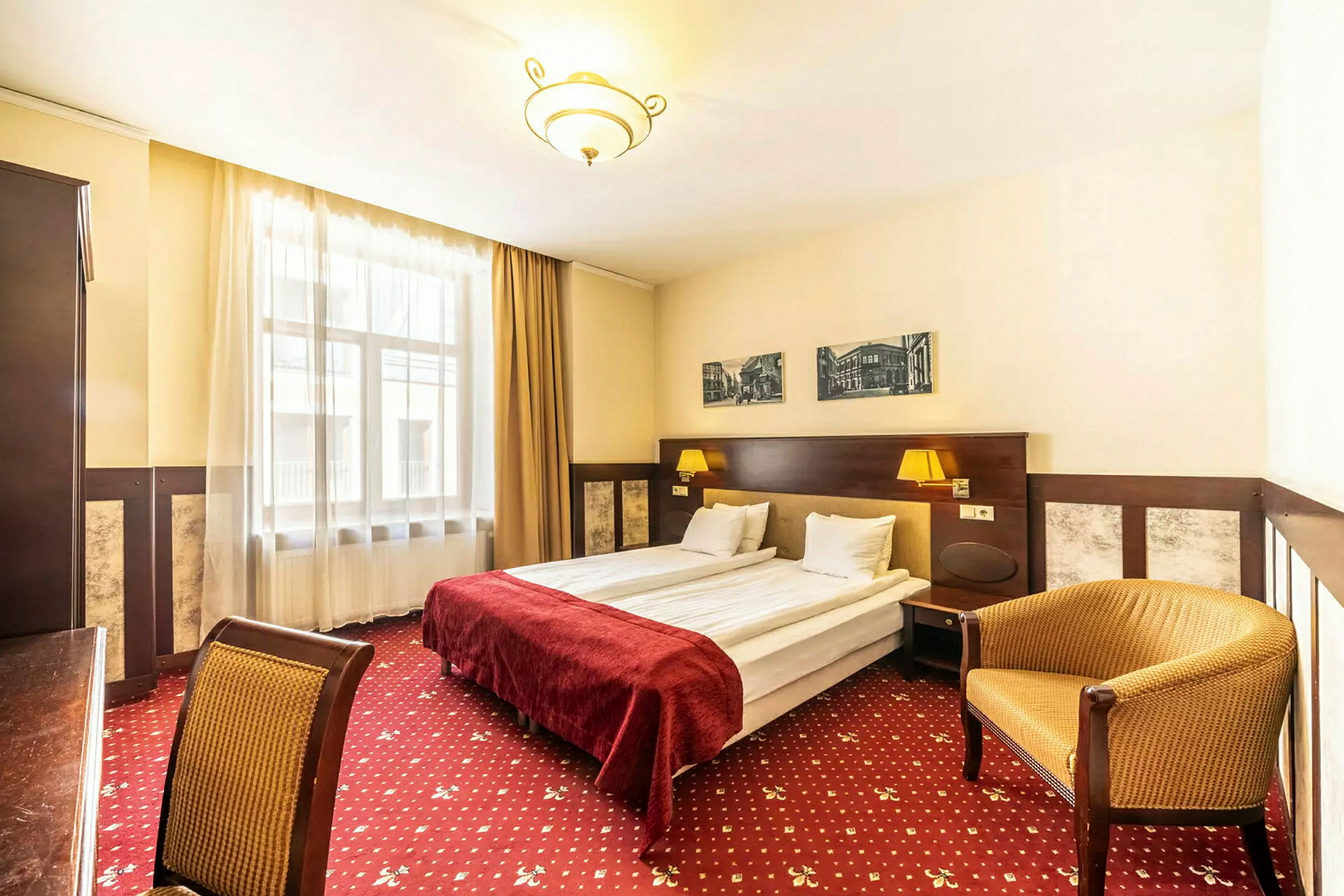 Ett hotellrum med dubbelsäng, röda sängkläder, väggdekorationer och stolar. (AI-genererad text)