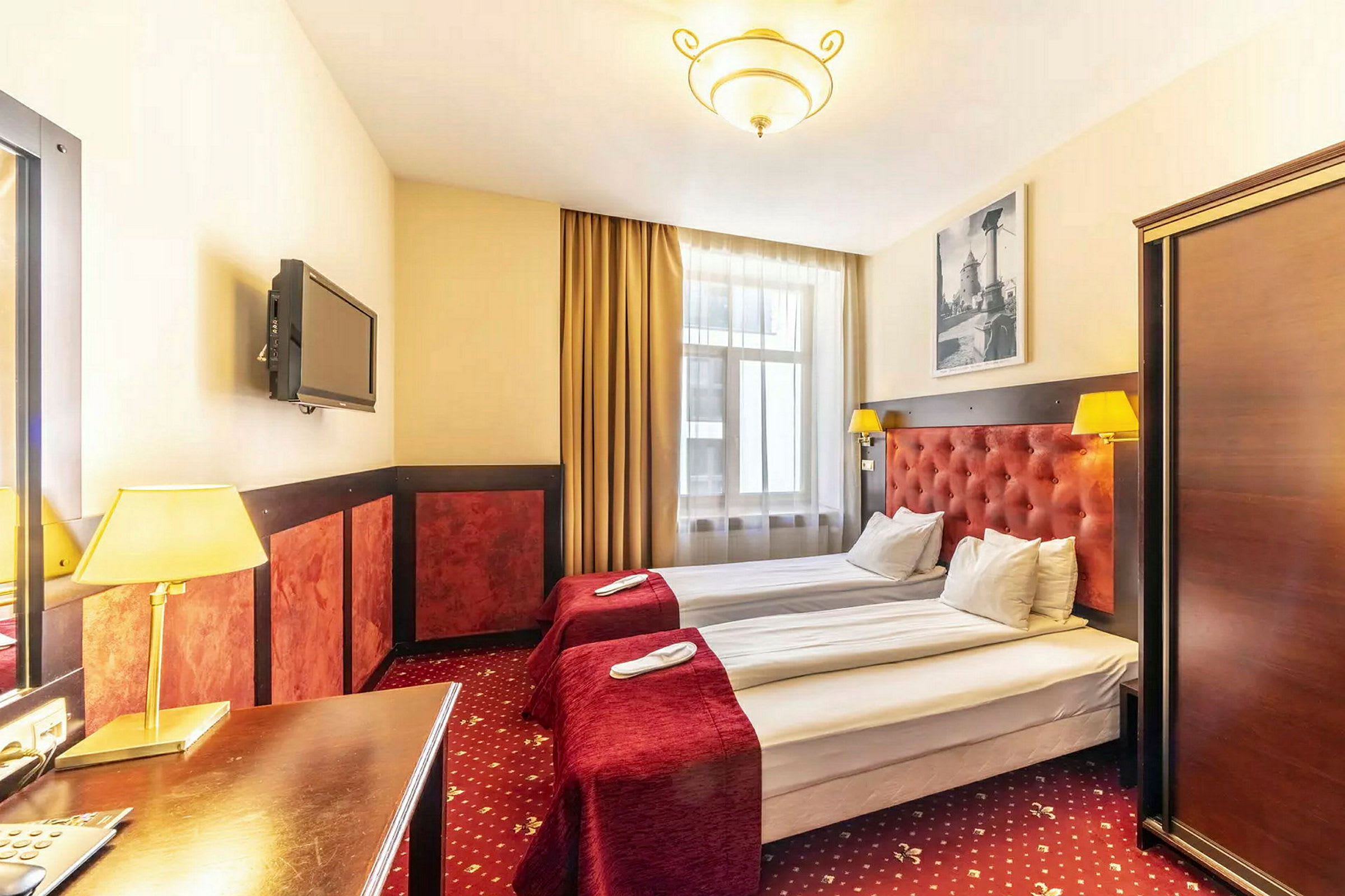 Hotellrum med två enkelsängar, röda sängöverkast och lampor. (AI-genererad text)