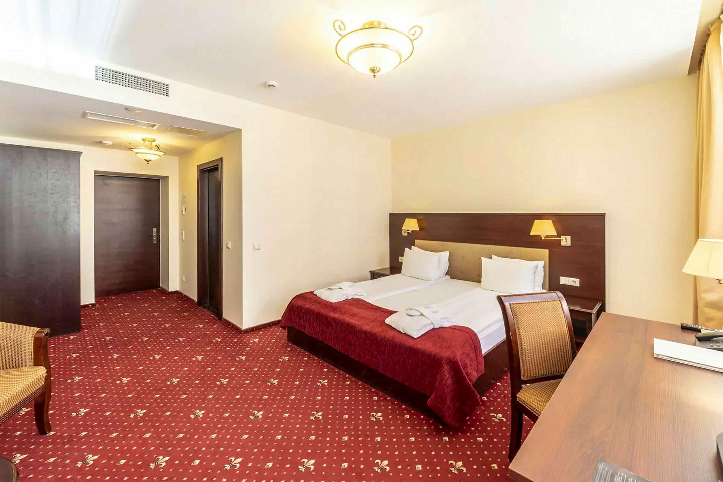 Hotellrum med dubbelsäng, skrivbord och stol. (AI-genererad text)