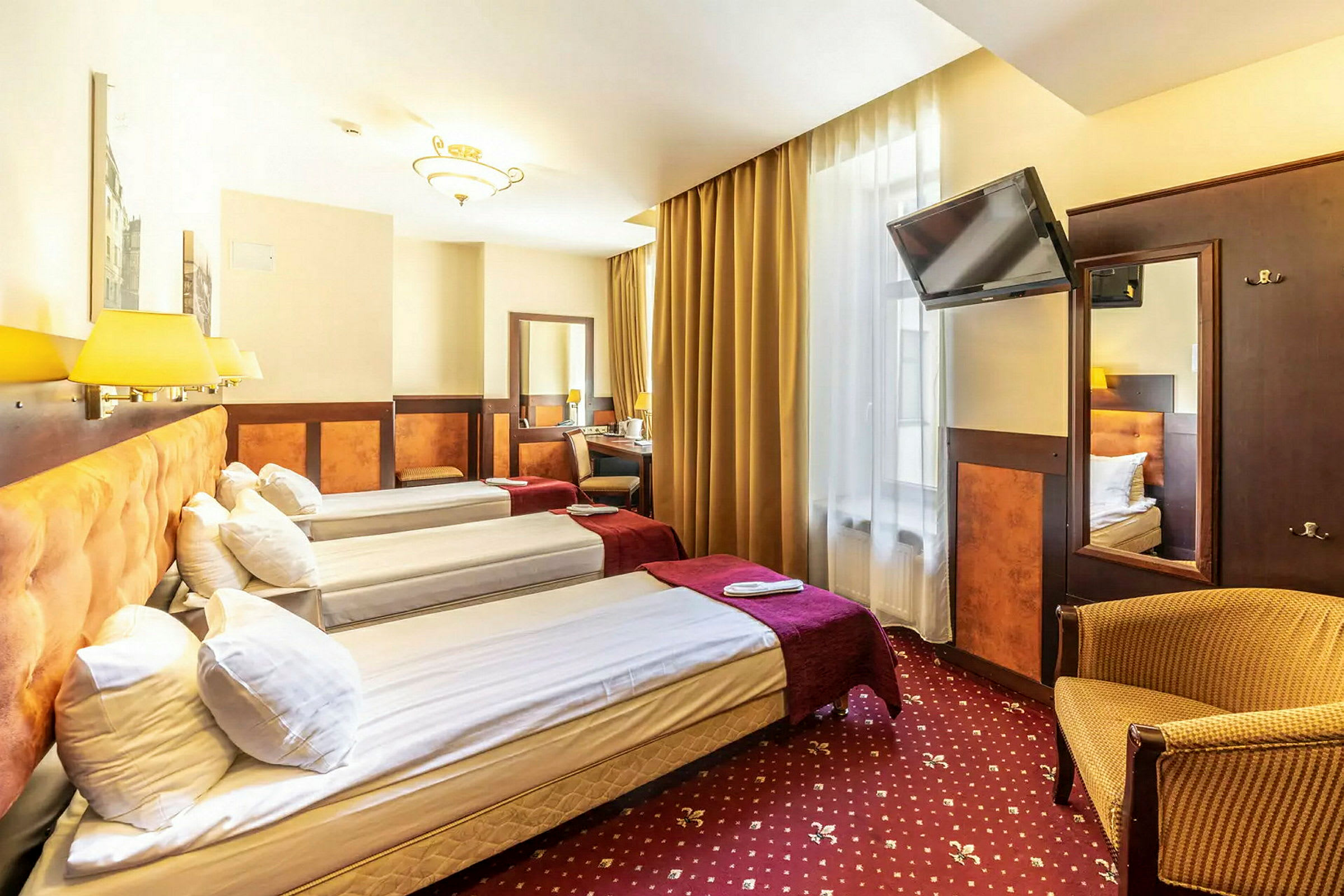 Hotellrum med tre enkelsängar, TV, skrivbord och fåtölj. (AI-genererad text)