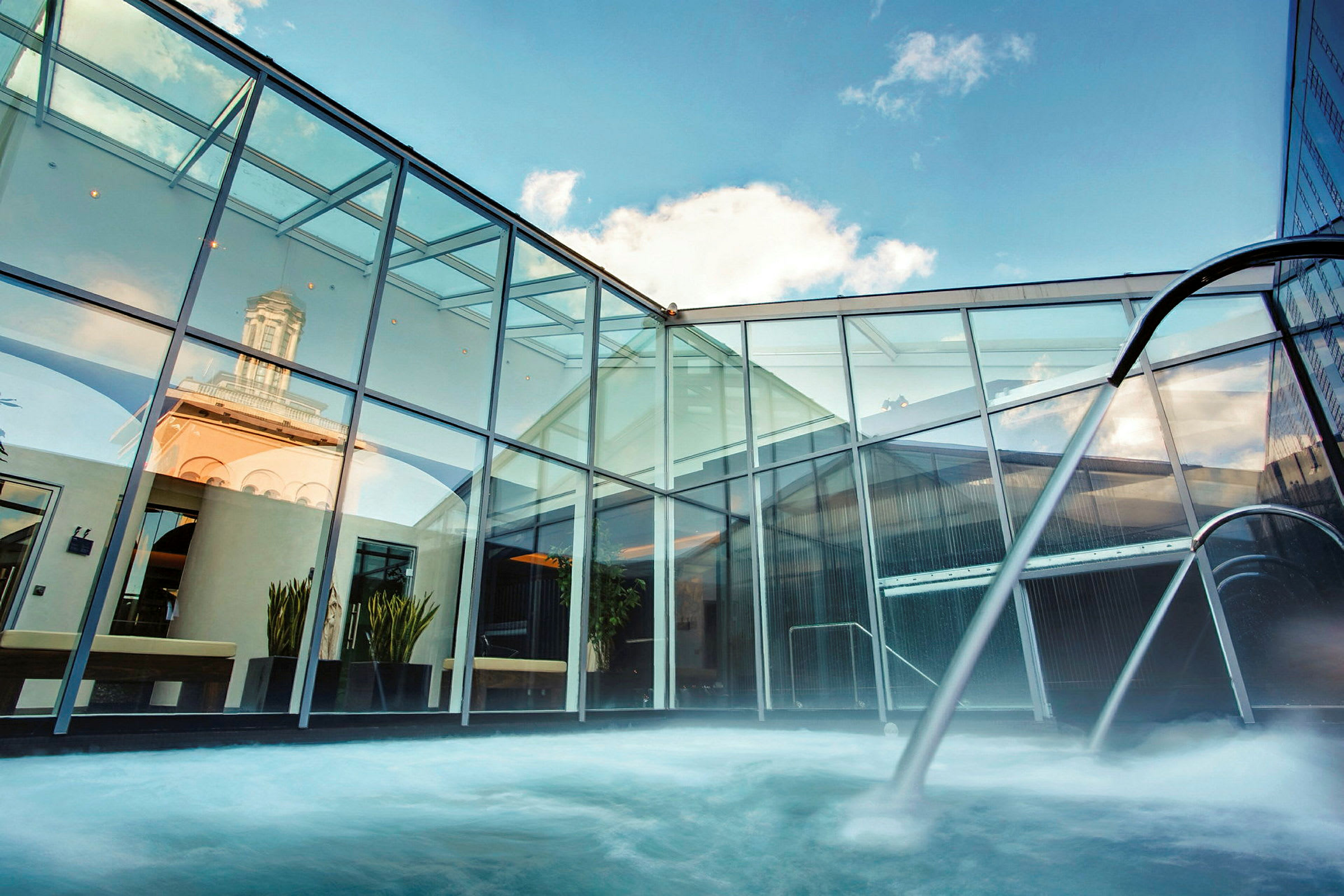 Ett modernt spa med en utomhuspool omgiven av glasväggar och himmel i bakgrunden. (AI-genererad text)