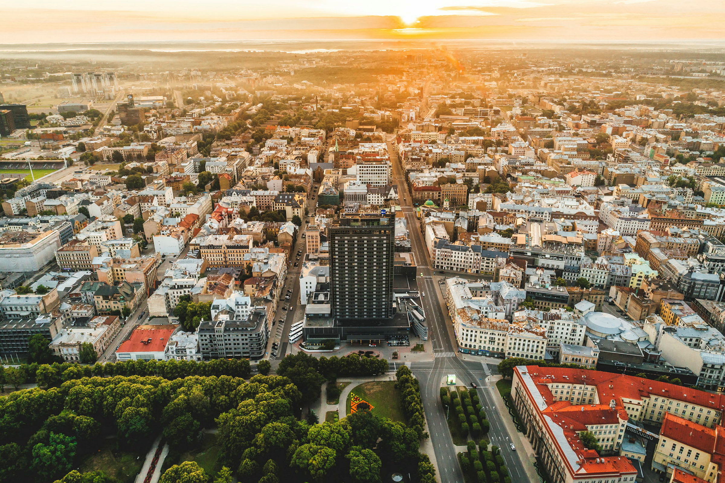 Flygbild över en stad med byggnader, vägar och parker i solnedgången. (AI-genererad text)