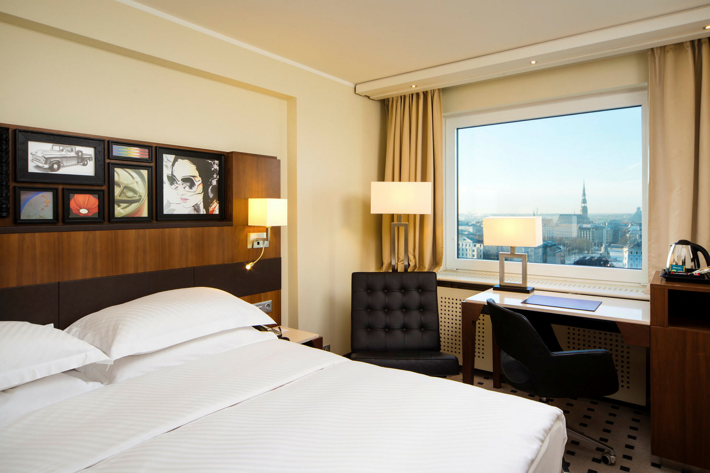Hotellrum med en stor säng, moderna möbler och ett stort fönster med utsikt över en stad. (AI-genererad text)