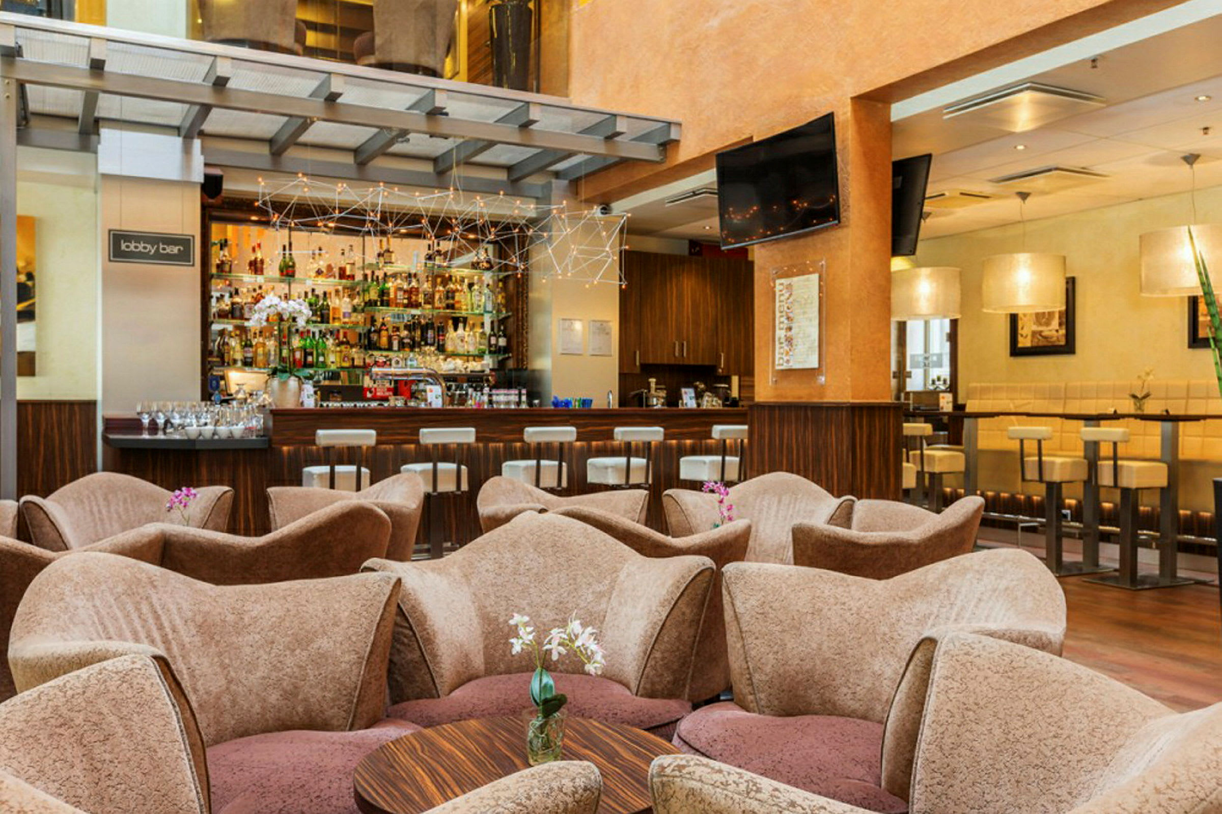 Bild av en lobbybar med soffor och ett bord i förgrunden, samt bar med flaskor och sittplatser i bakgrunden. (AI-genererad text)