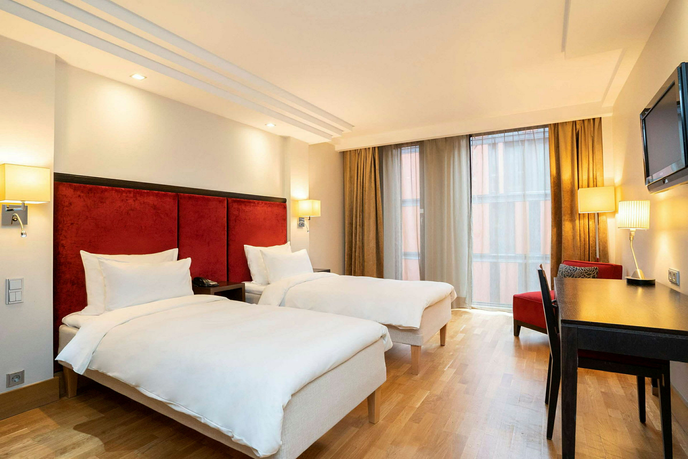 Ett hotellrum med två enkelsängar, skrivbord, stol och ett stort fönster med gardiner. (AI-genererad text)