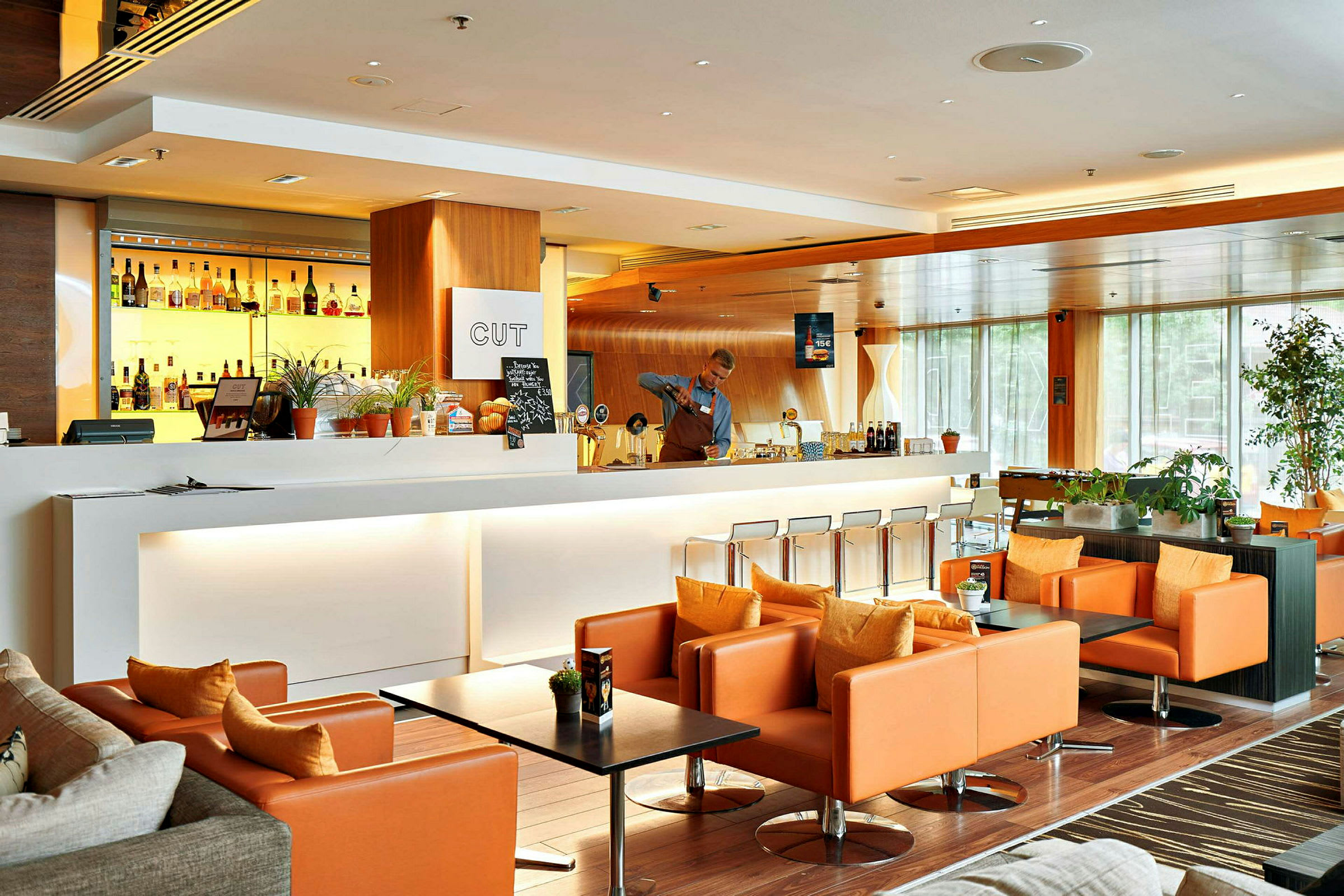 En modern och elegant lounge med en vit bardisk, bakgrundsbelysta spritflaskor och bekväma orange fåtöljer. (AI-genererad text)