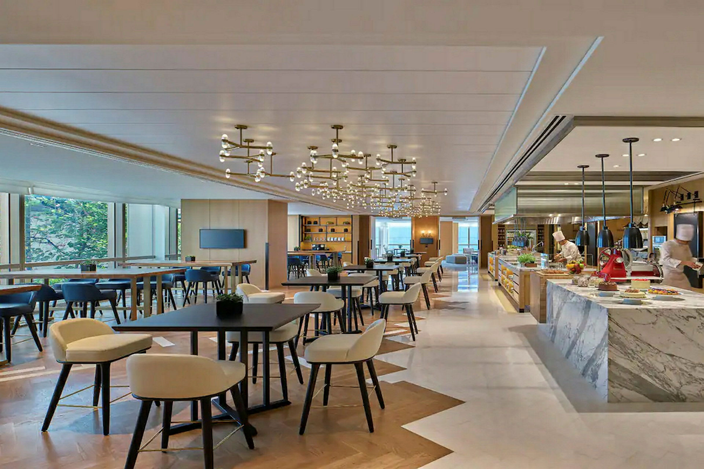 En modern restaurang med bord, stolar och ett köksområde där två personer arbetar. (AI-genererad text)