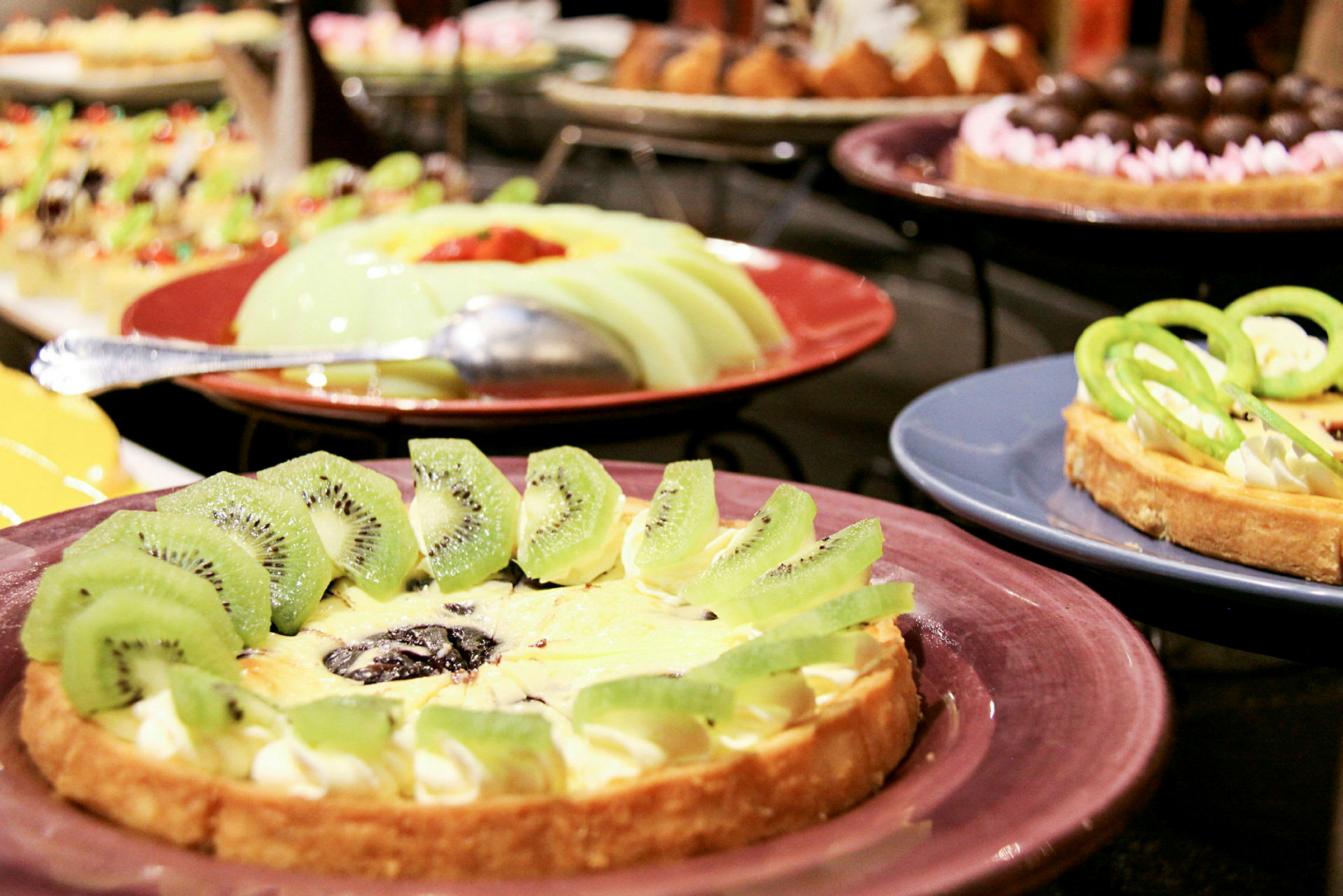 Olika desserter, inklusive en paj dekorerad med kiwi på en tallrik. (AI-genererad text)