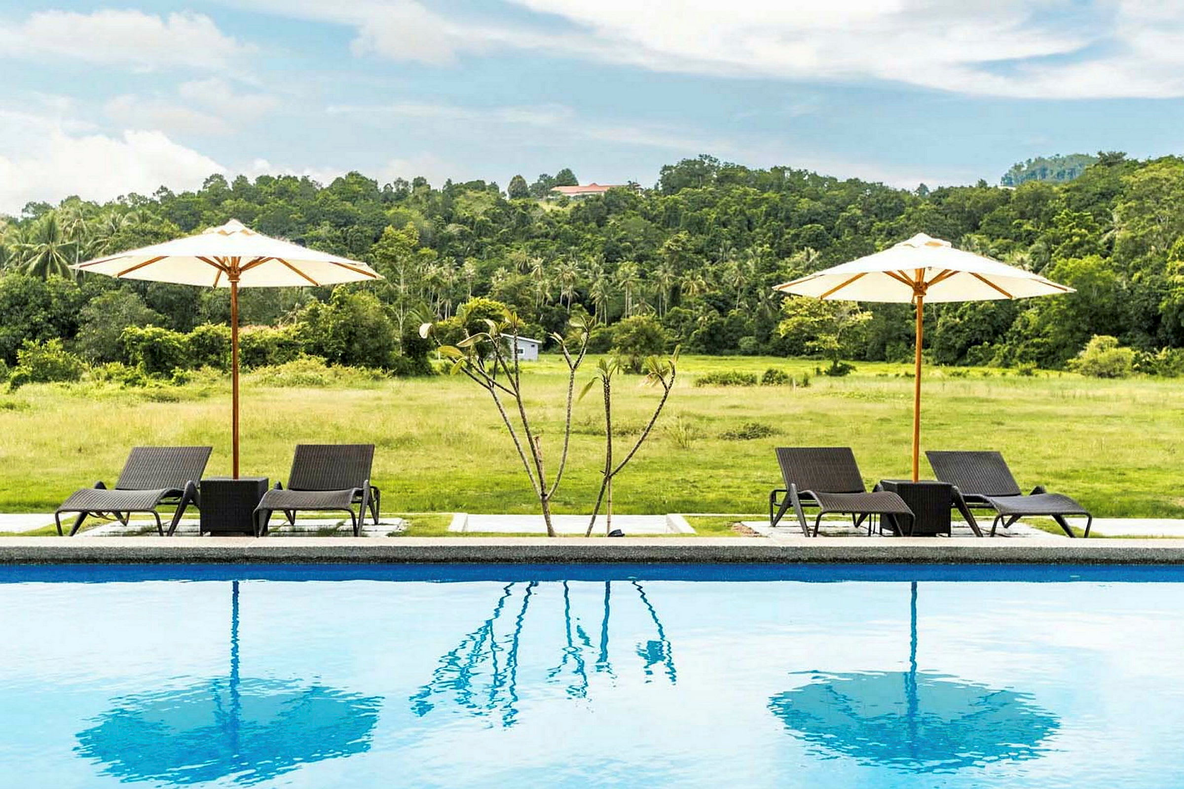 En pool med solstolar och parasoller i en grönskande utomhusmiljö. (AI-genererad text)