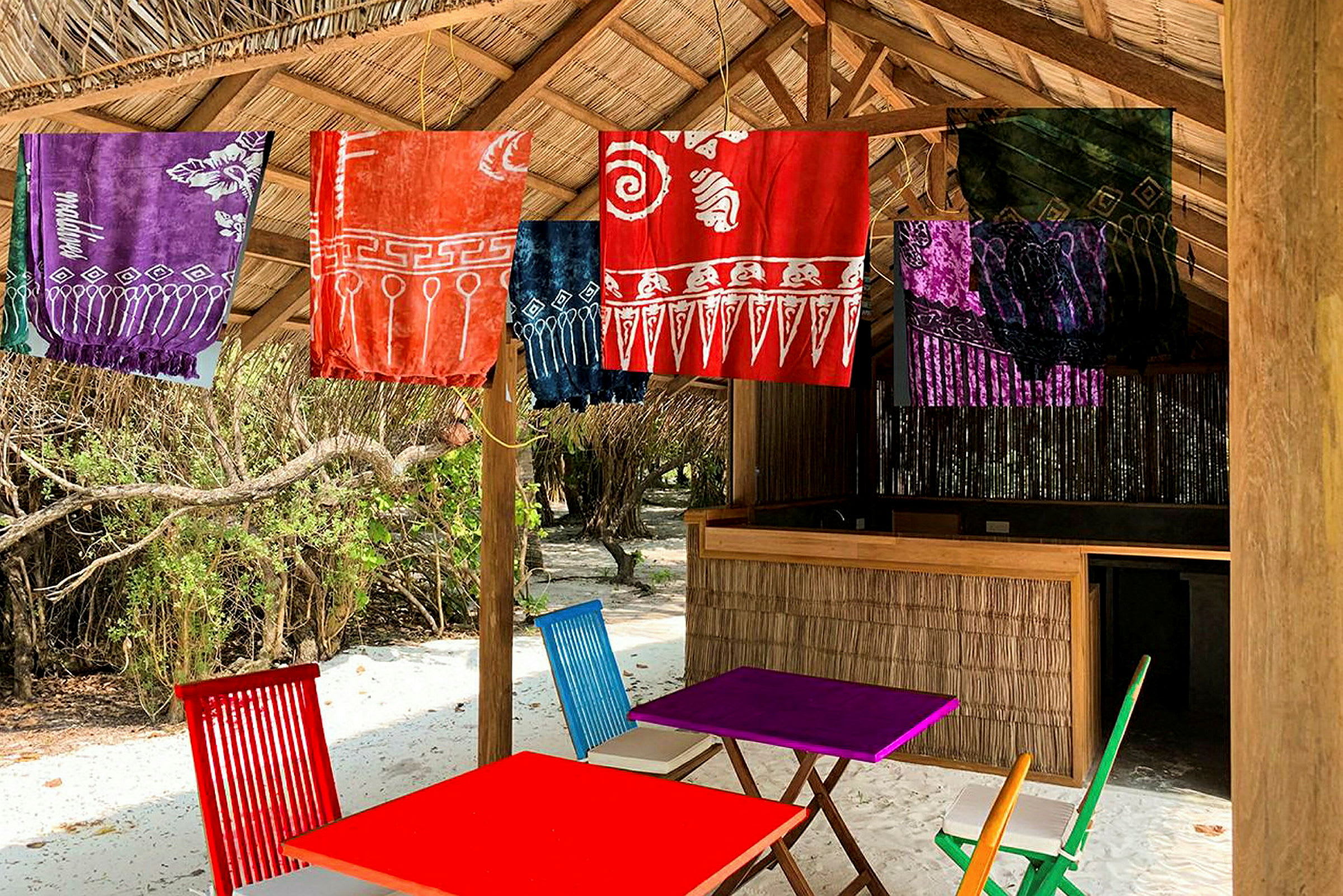 Strandbar med färgglada textilier som hänger under halmtak. (AI-genererad text)
