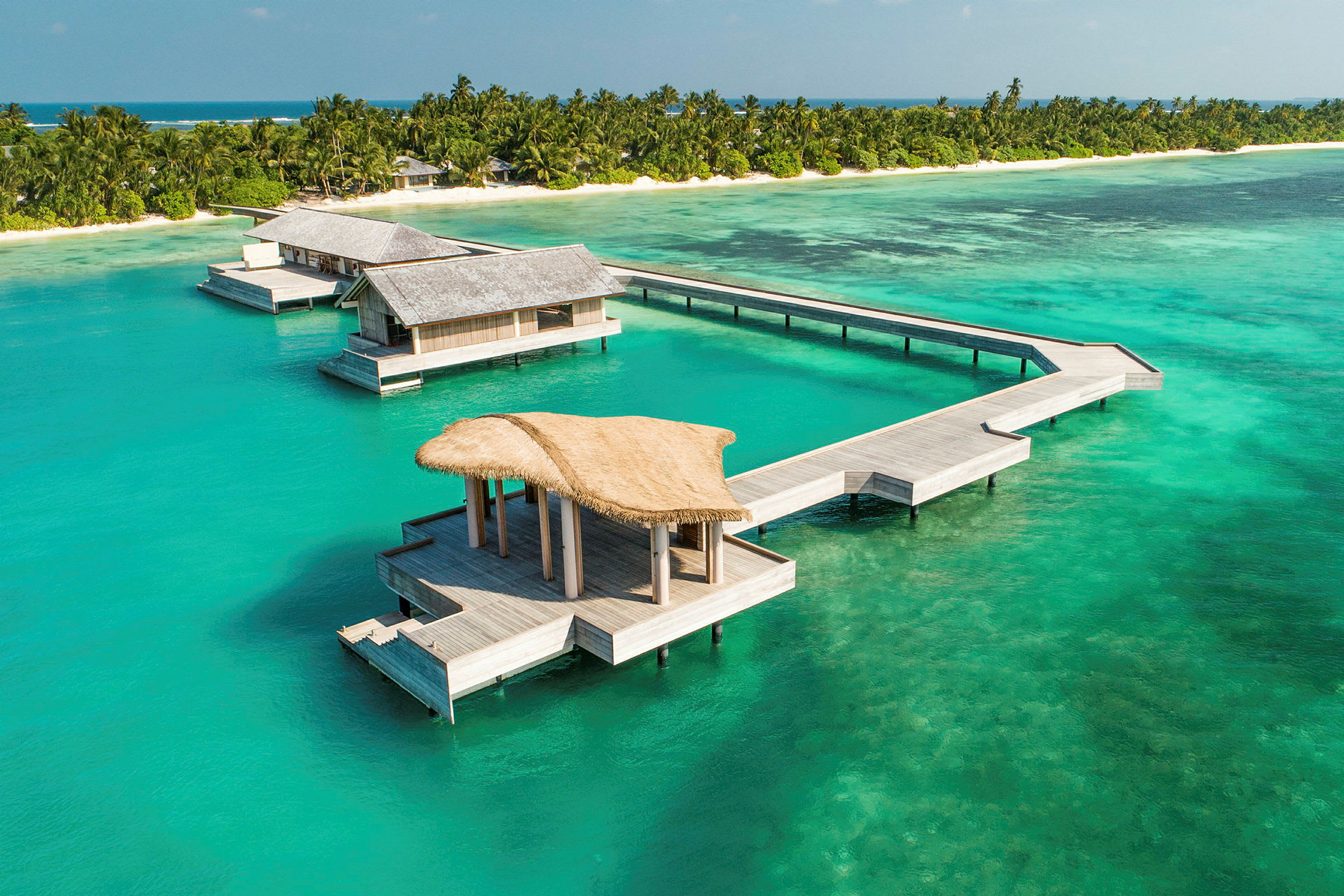 Övervattensbungalower vid en tropisk strand med turkost hav. (AI-genererad text)