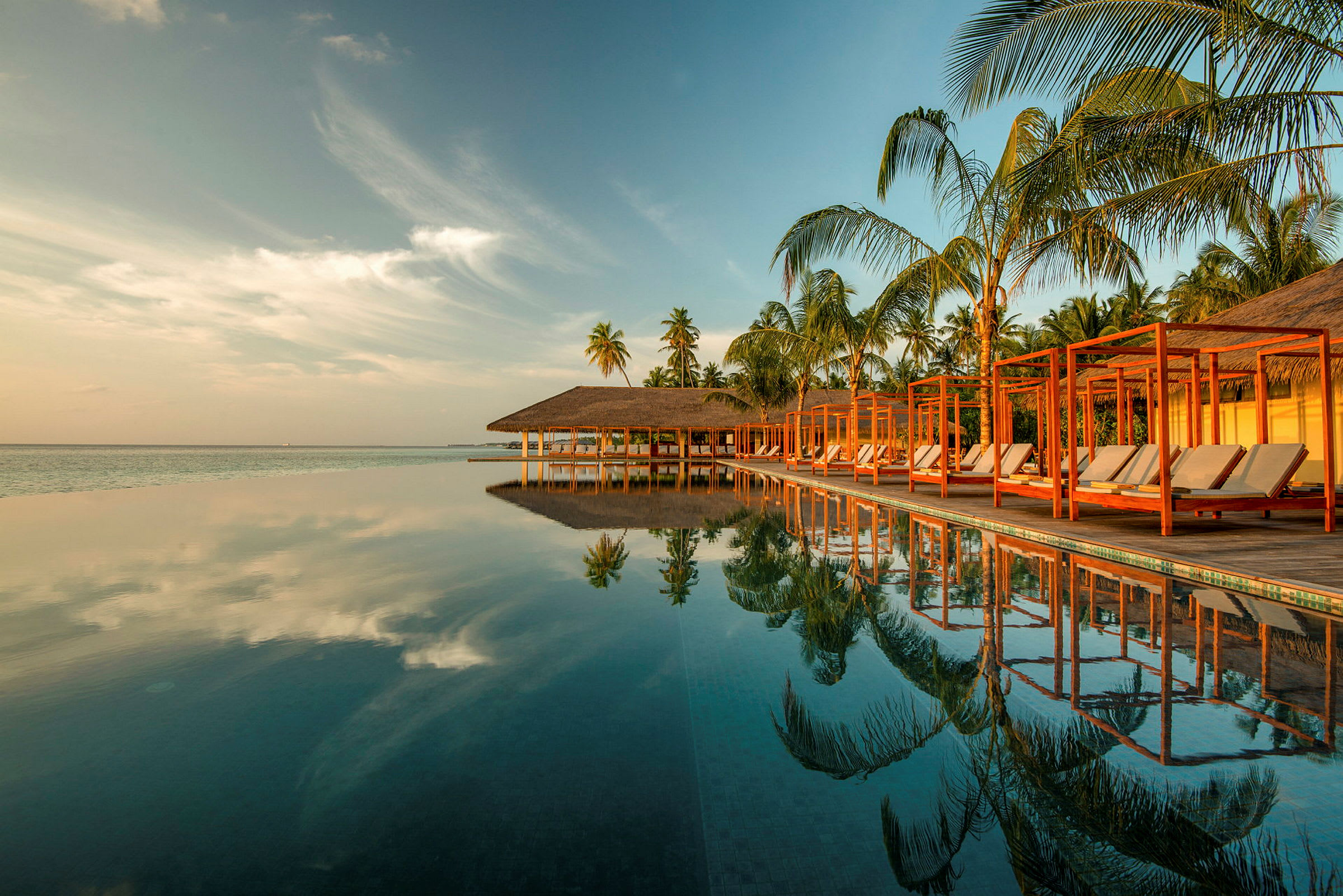 En infinitypool vid en tropisk resort med palmer och himmel som speglas i vattnet. (AI-genererad text)