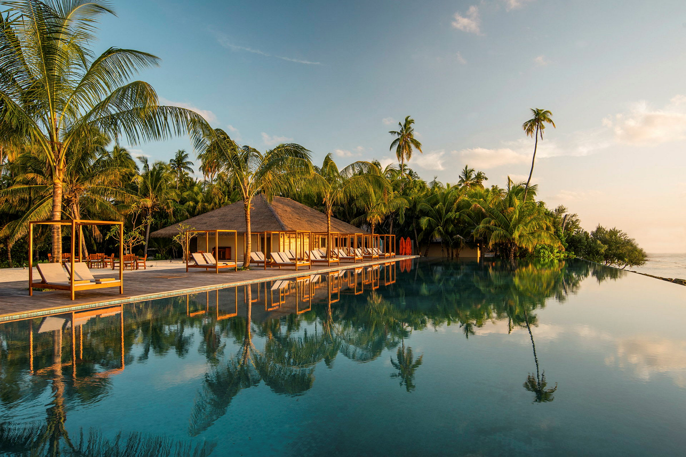 Bild av en tropisk resort med en infinitypool, omgiven av palmer och strandnära byggnader. (AI-genererad text)