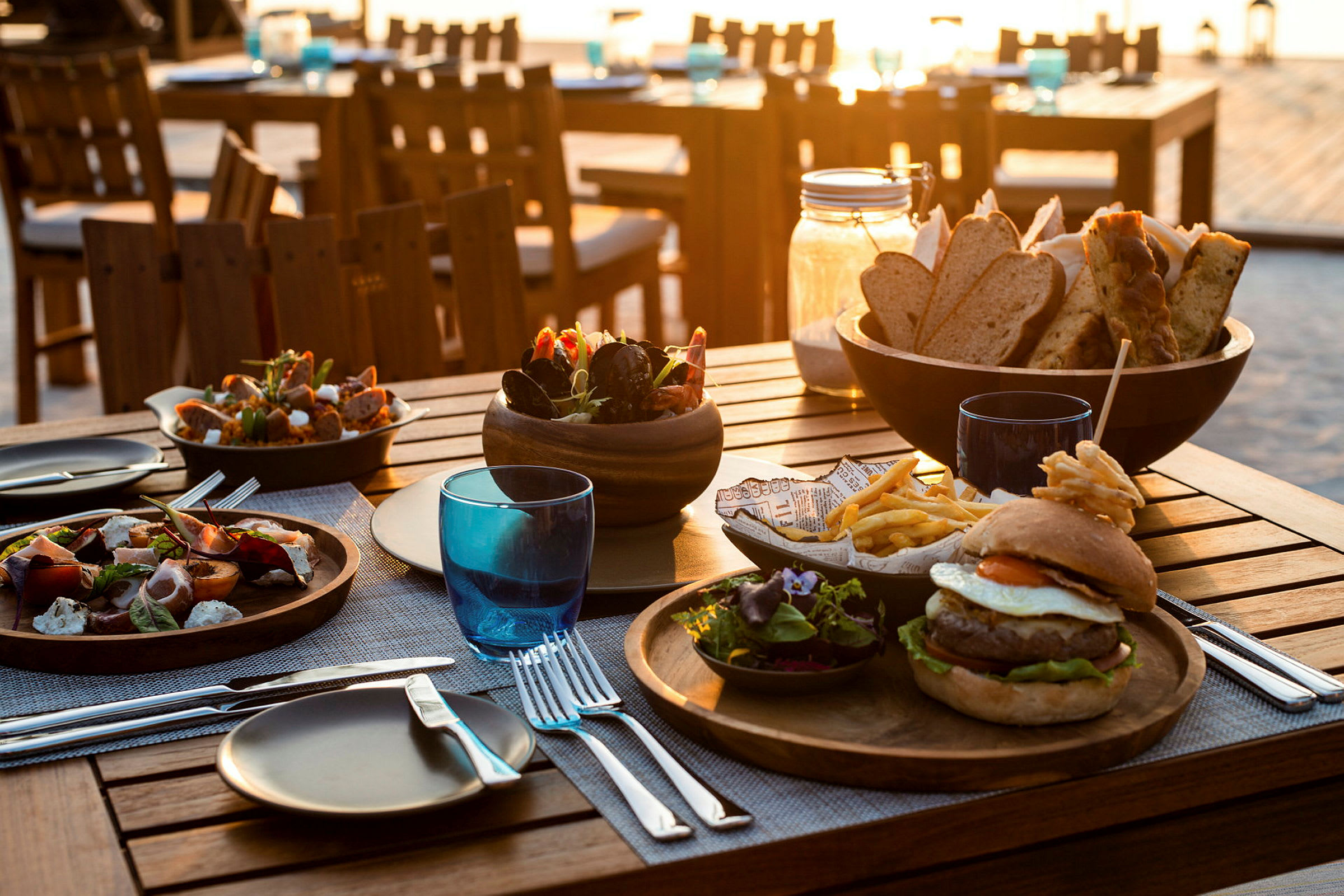 Middag serverad vid ett bord utomhus med olika maträtter och drycker. (AI-genererad text)