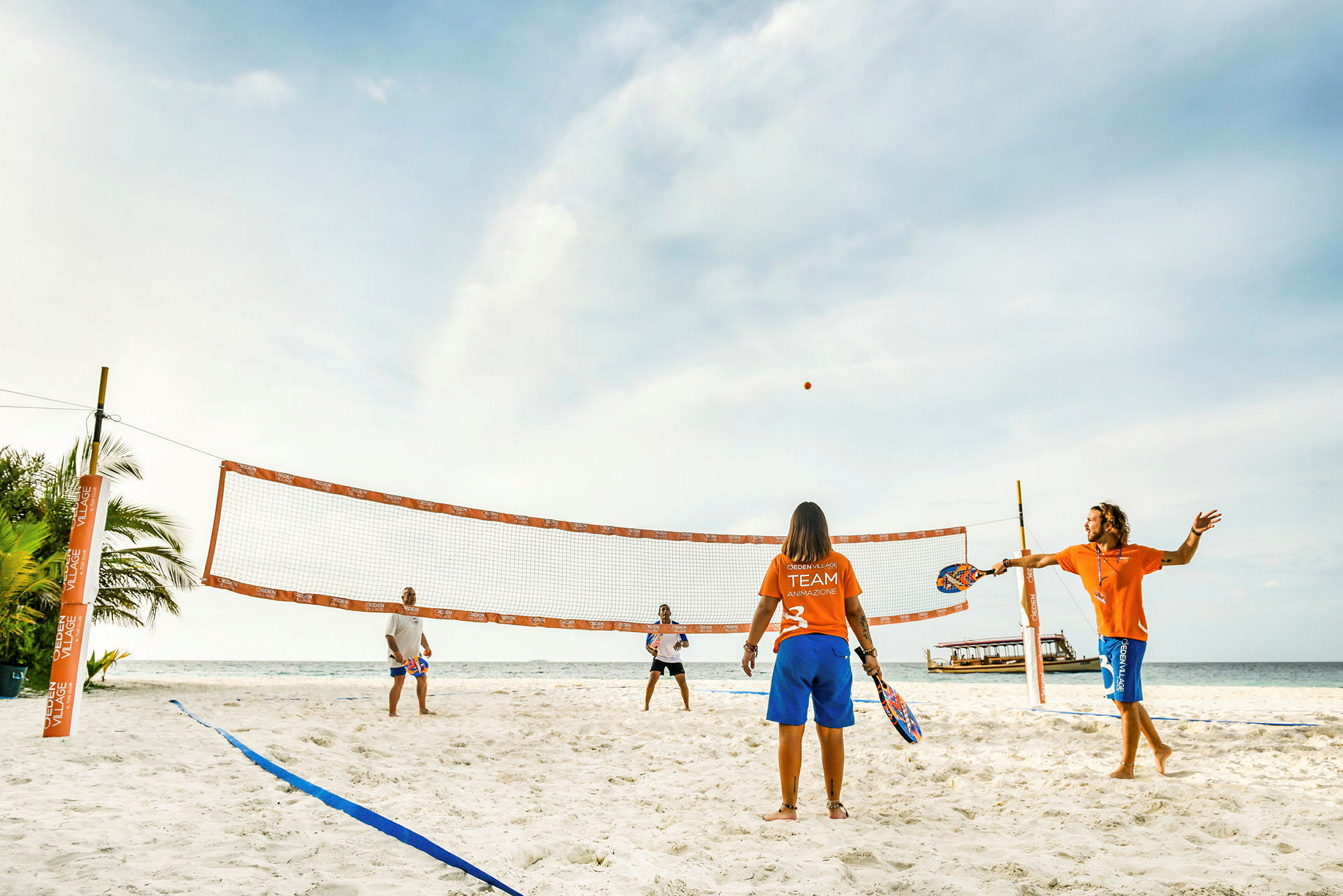 Fyra personer spelar strandtennis på en solig sandstrand. (AI-genererad text)