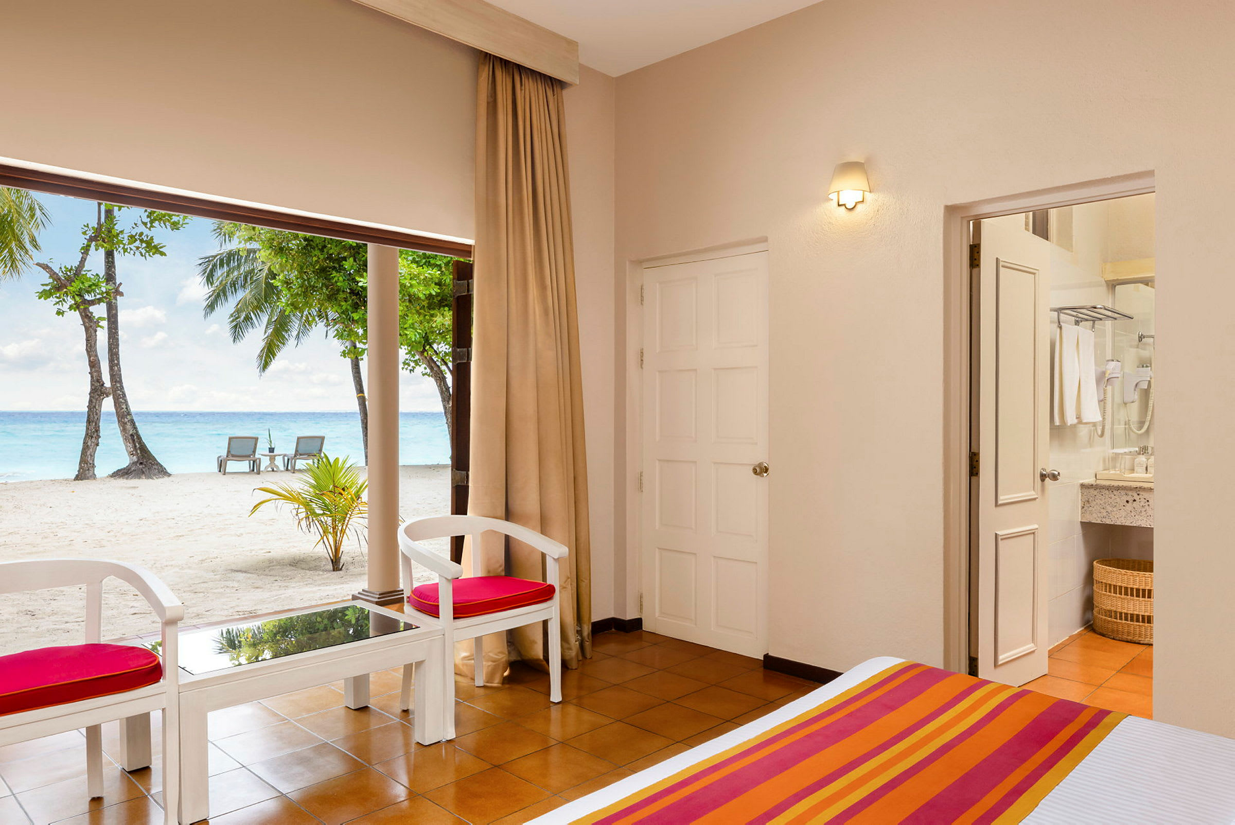 Ett hotellrum med utsikt över en strand med två solstolar och palmer. (AI-genererad text)