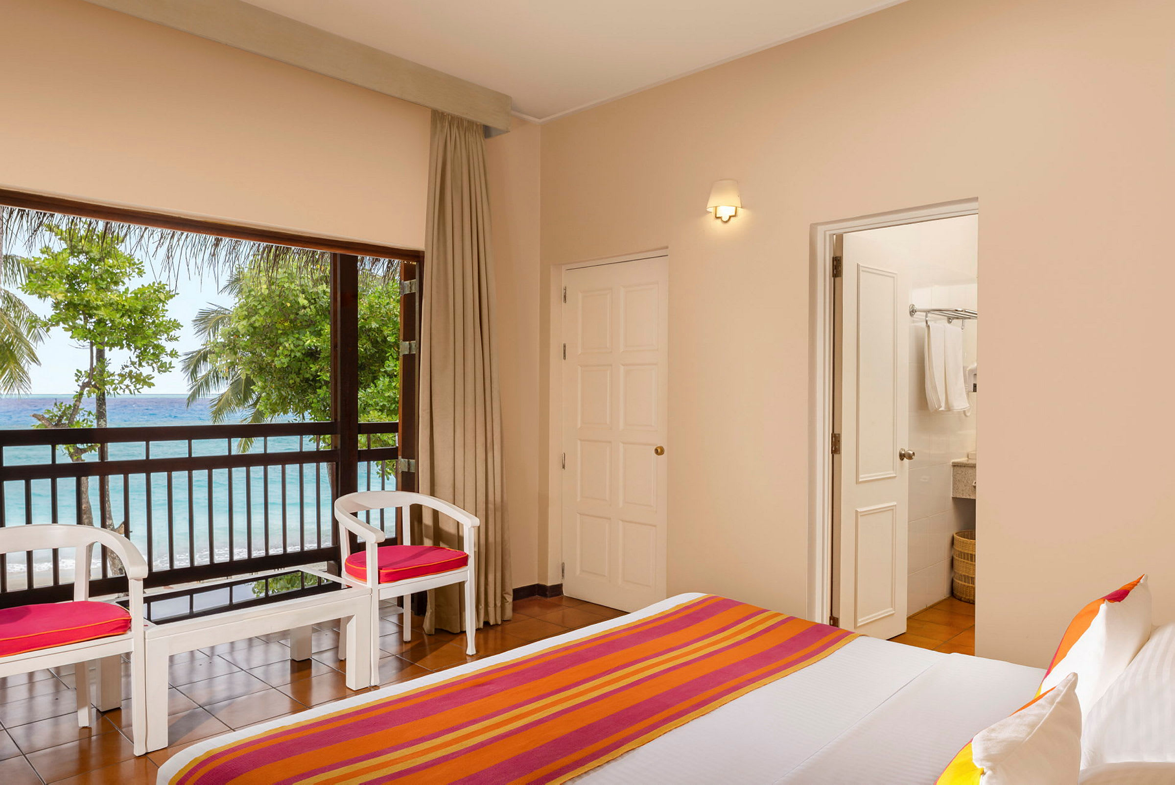 Ett hotellrum med säng och möbler i trä, utsikt mot havet och grönska utanför fönstret. (AI-genererad text)