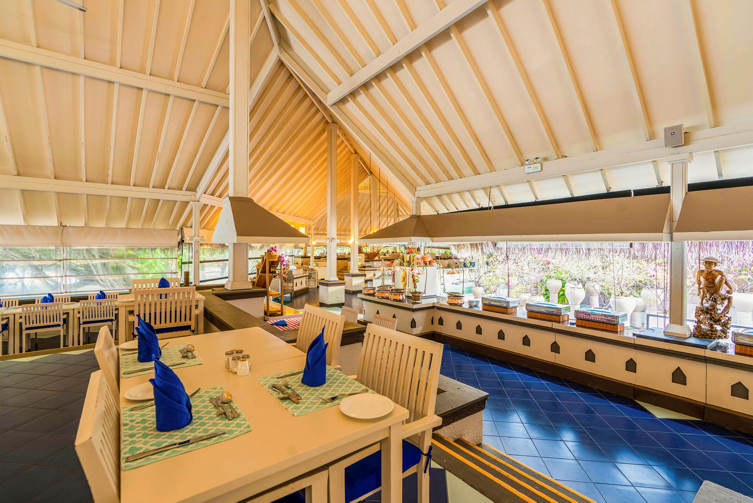 Interiör av en restaurang med dukade bord, blå servetter och en buffé i bakgrunden. (AI-genererad text)