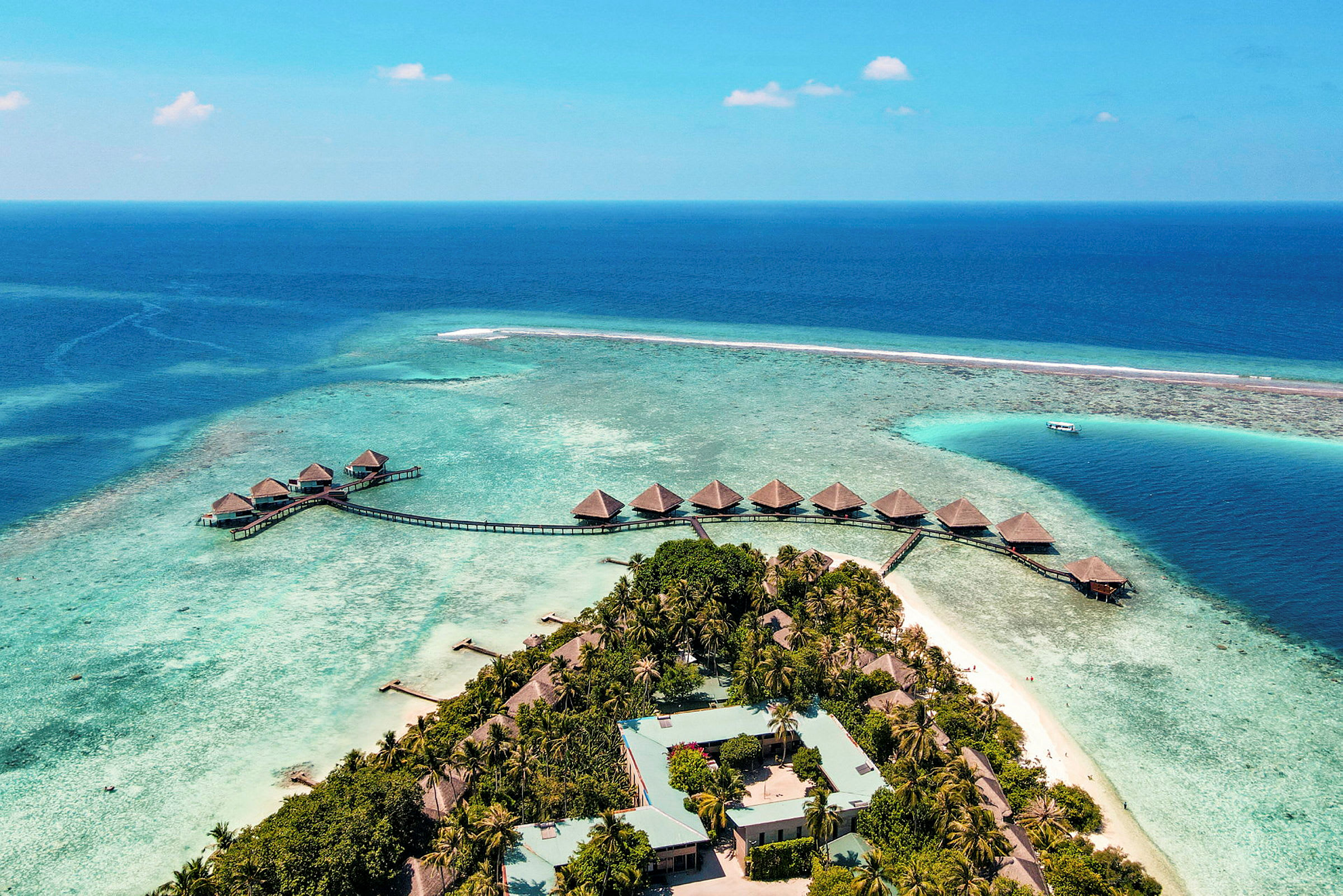 Flygbild över ett tropiskt semesterresort med bungalower på vattnet. (AI-genererad text)