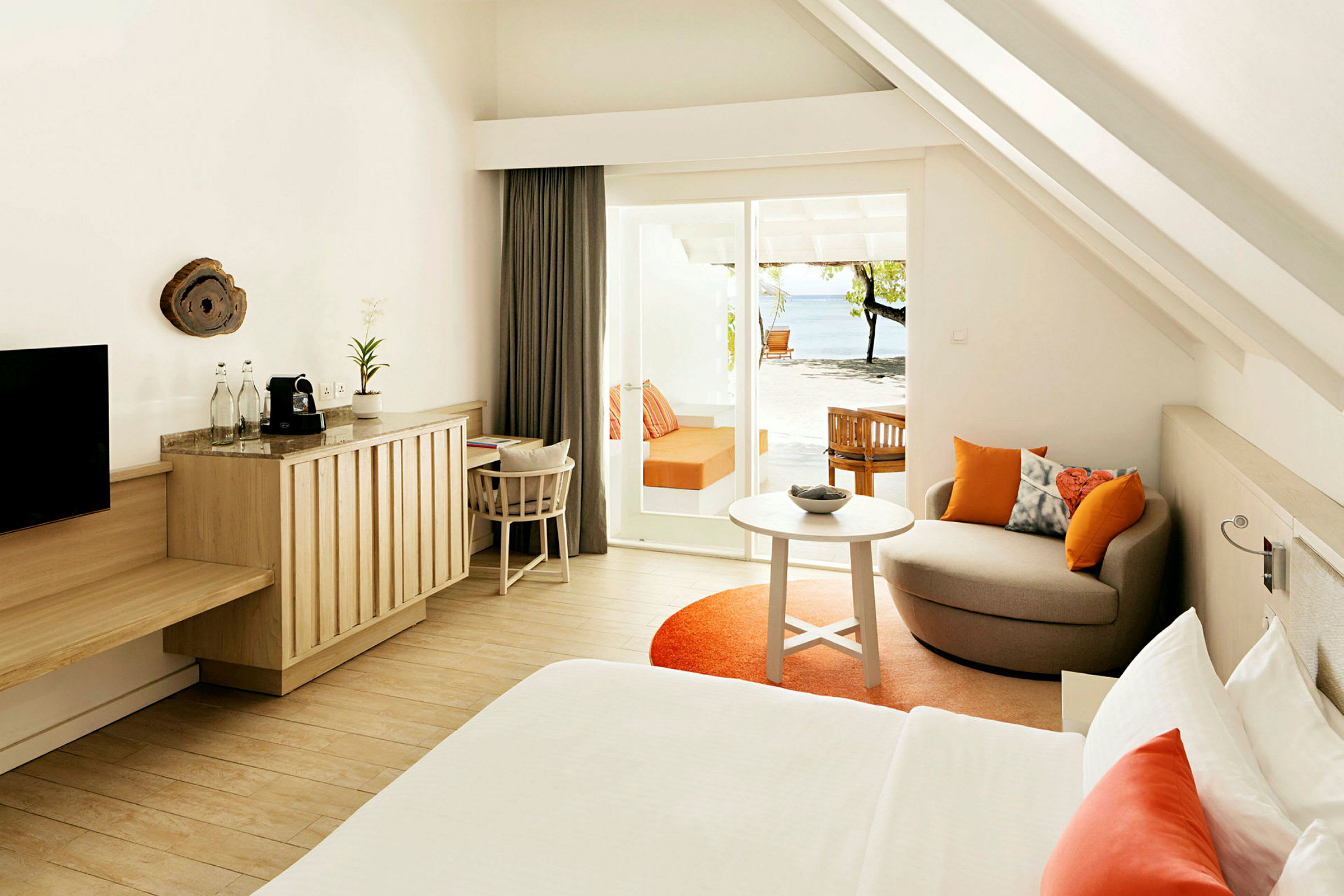 Ett modernt hotellrum med ljusa trädetaljer, orange accentfärger och en terrass med utsikt över stranden. (AI-genererad text)