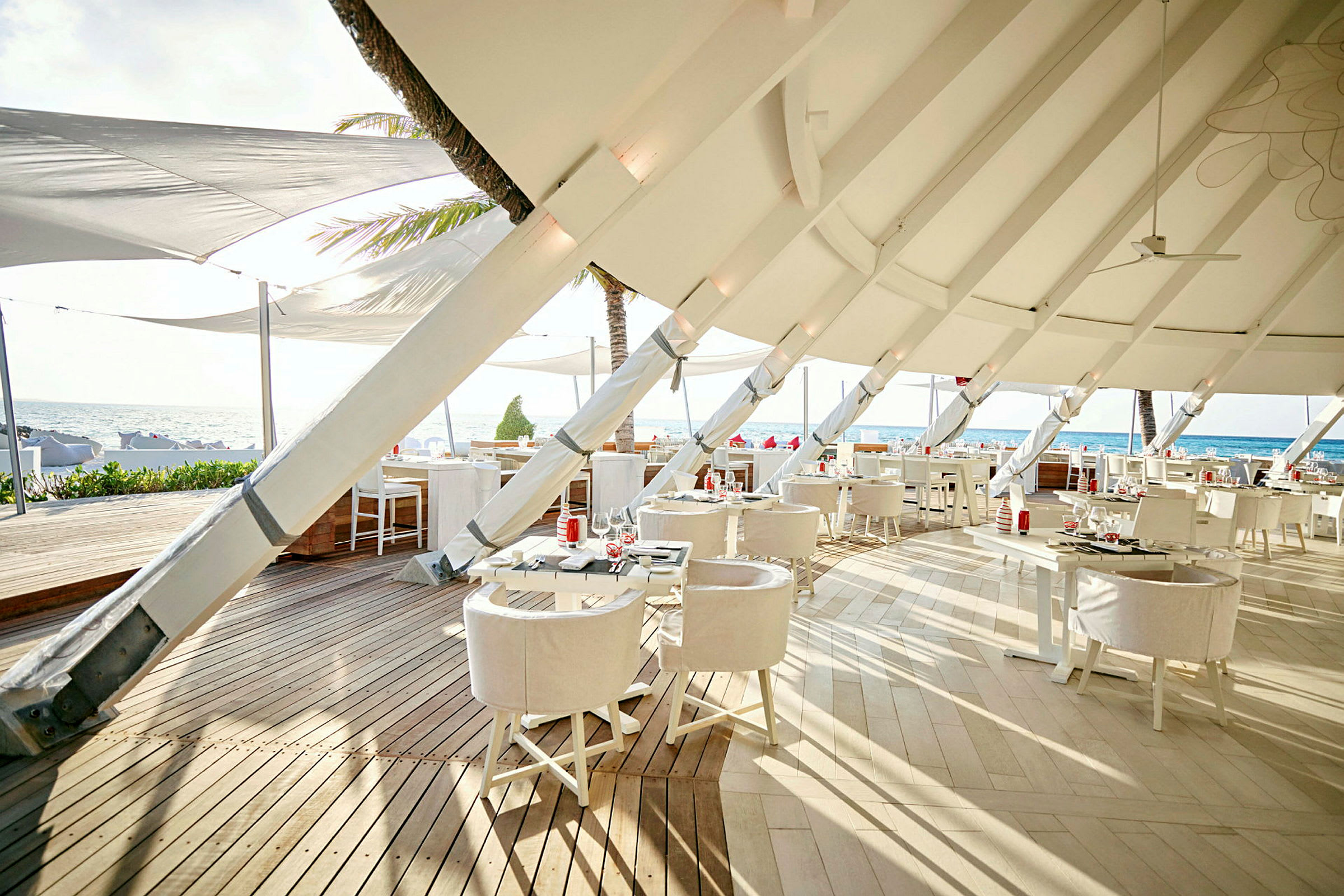 Restaurang med moderna vita möbler och takduk vid stranden. (AI-genererad text)