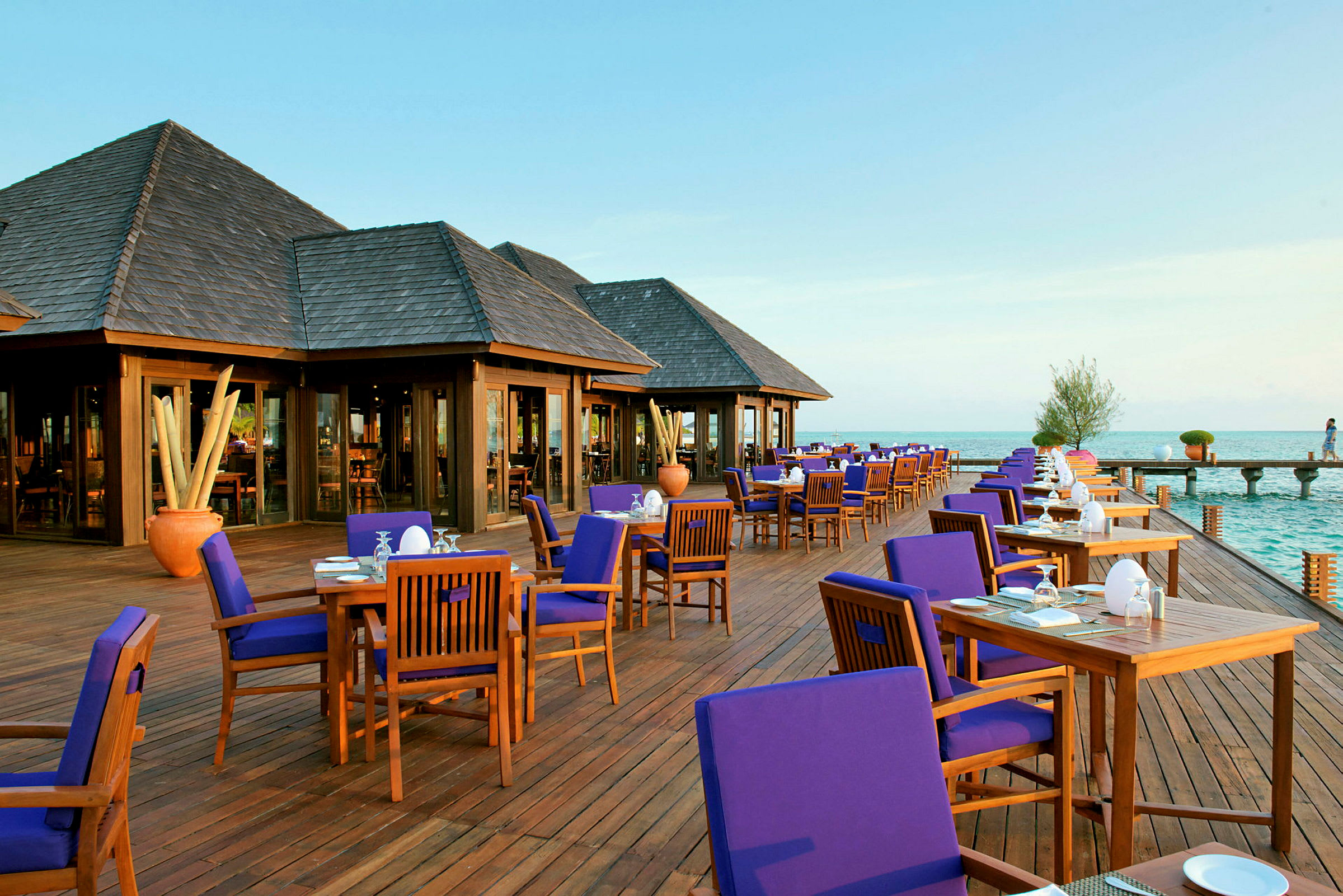 En utomhusrestaurang med trädeck och bord med blå stolar vid havet. (AI-genererad text)