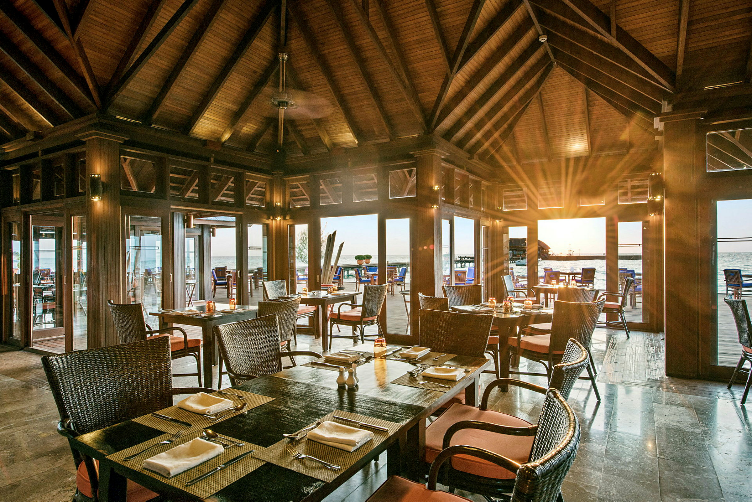 Restaurang med träinredning och dukade bord, med utsikt mot havet genom glaspartier. (AI-genererad text)