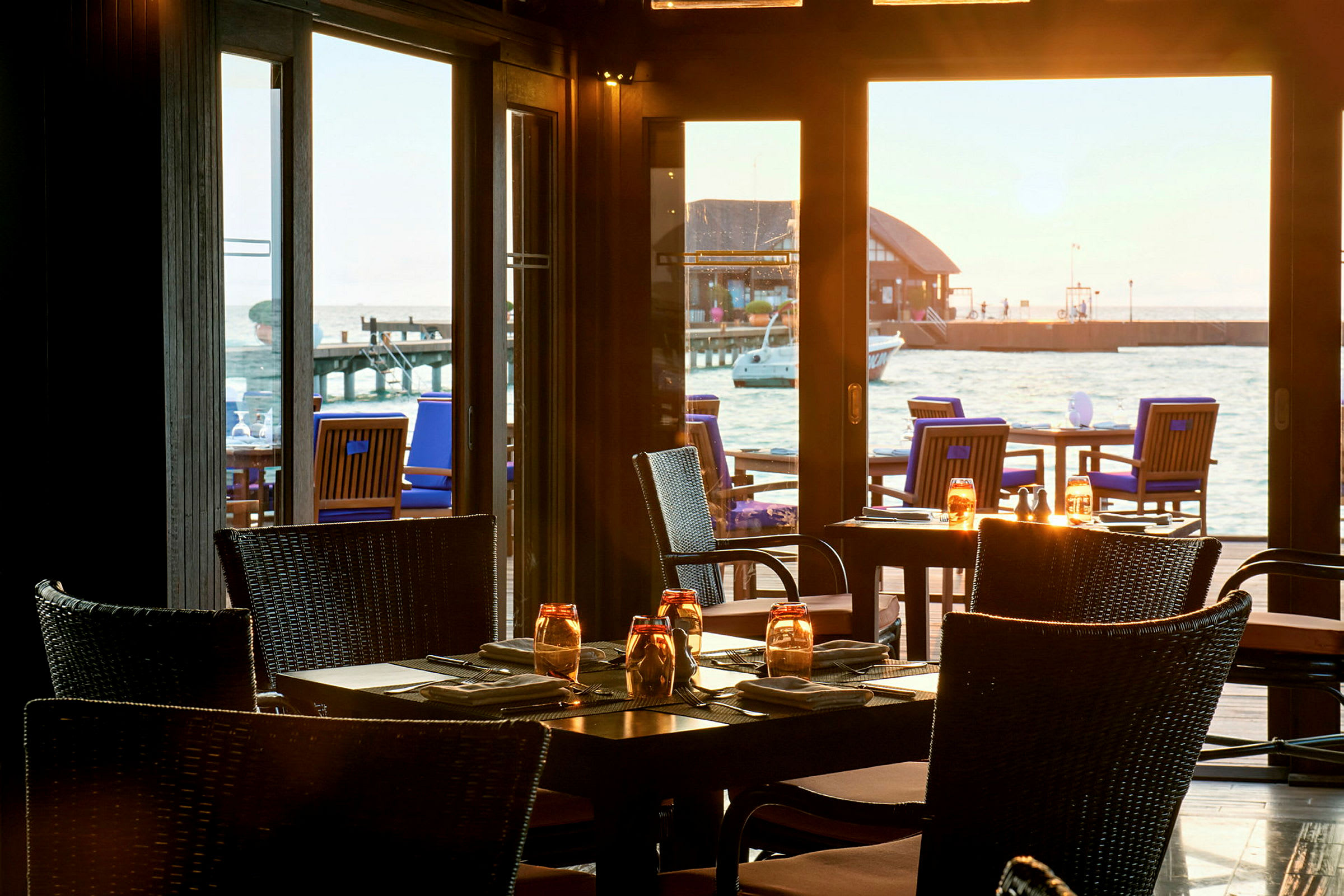Restaurang med bord och stolar inomhus samt havsutsikt från fönster. (AI-genererad text)