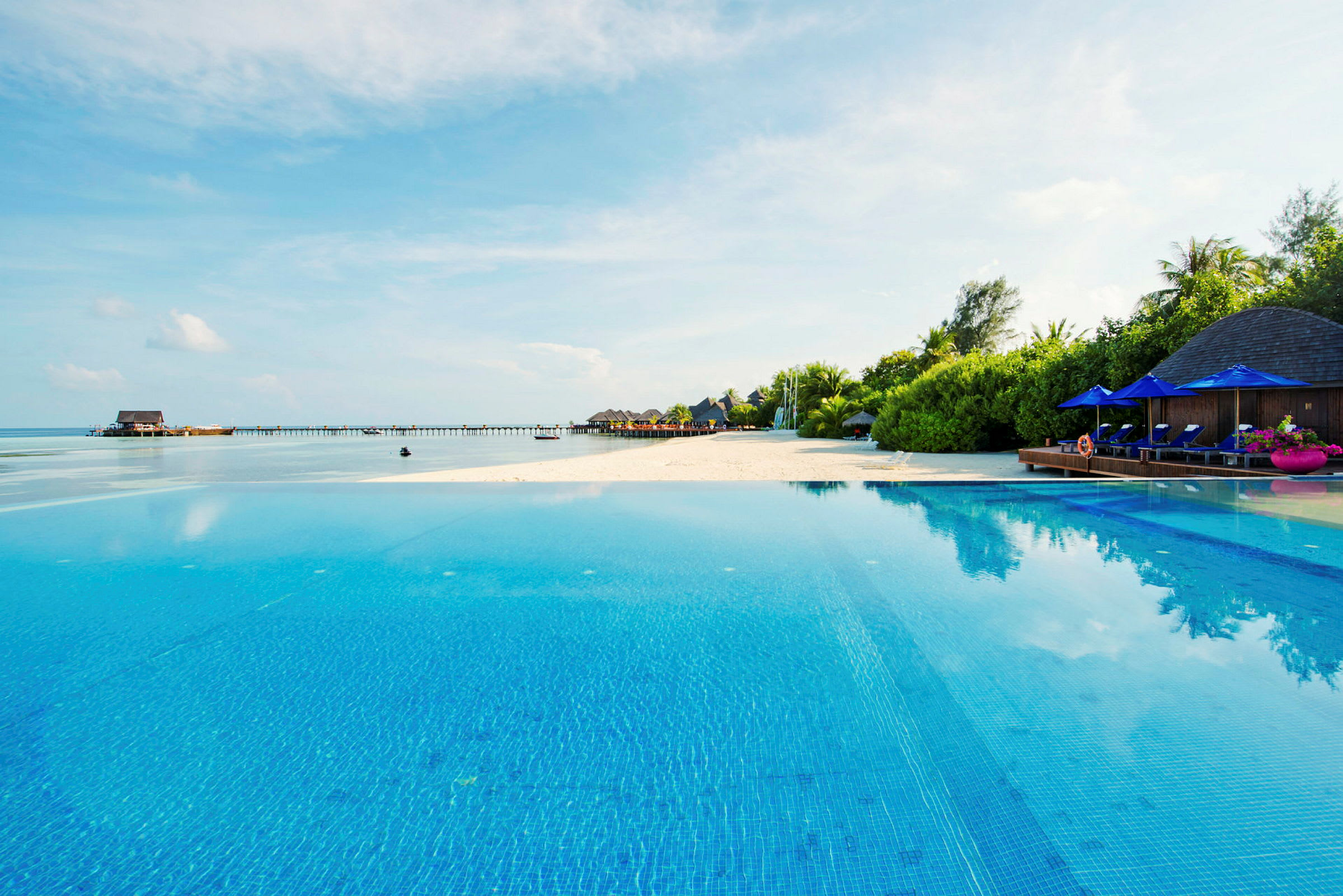 En pool med utsikt över stranden och havet, med solstolar och parasoller i bakgrunden. (AI-genererad text)